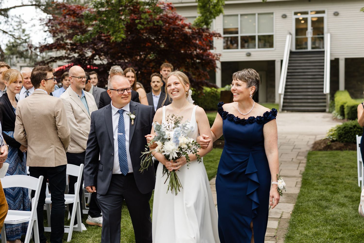 Wedding party members walk together after the ceremony on a landscaped garden path.