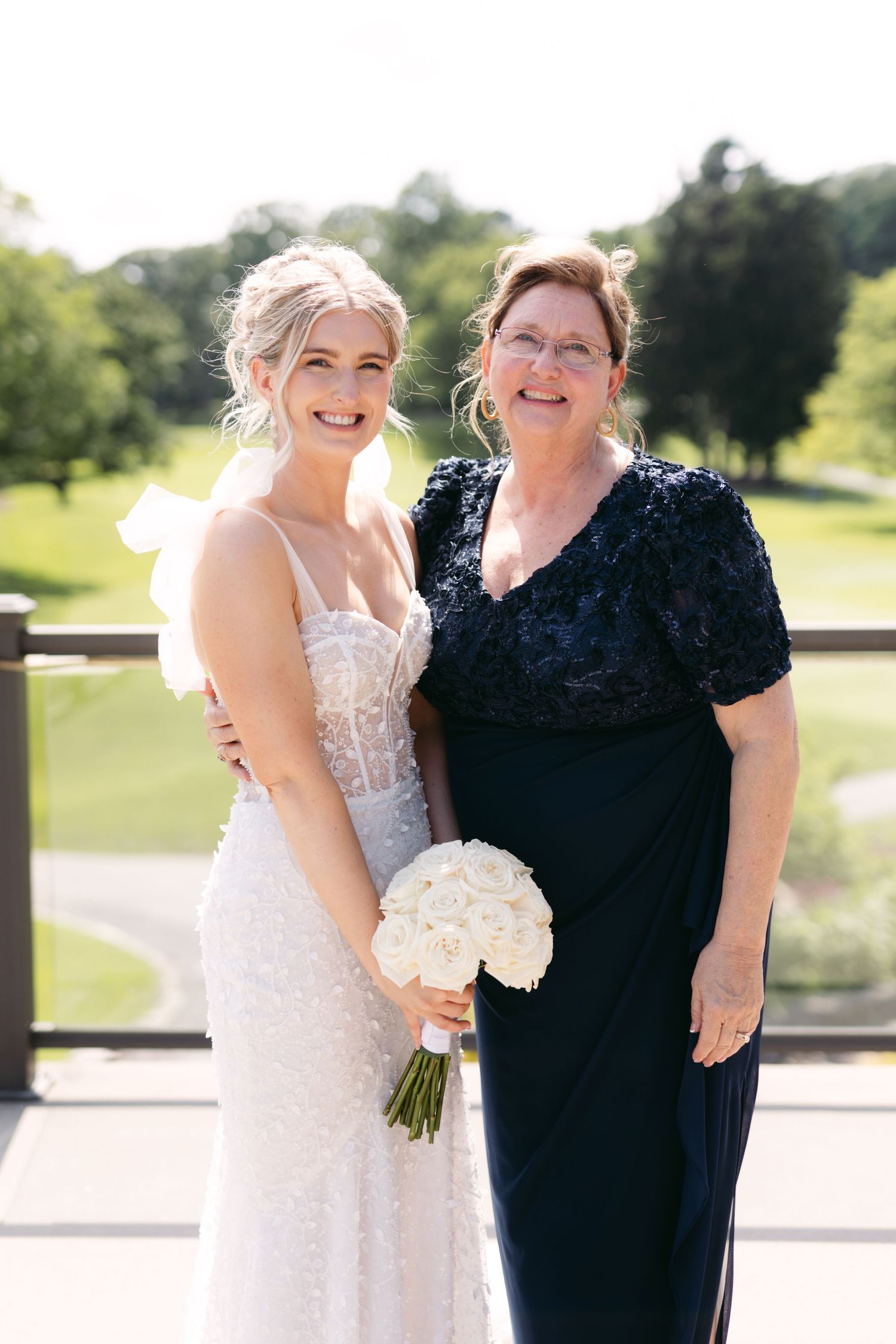 Bride in a lace wedding dress poses with family members for formal portraits outdoors.
