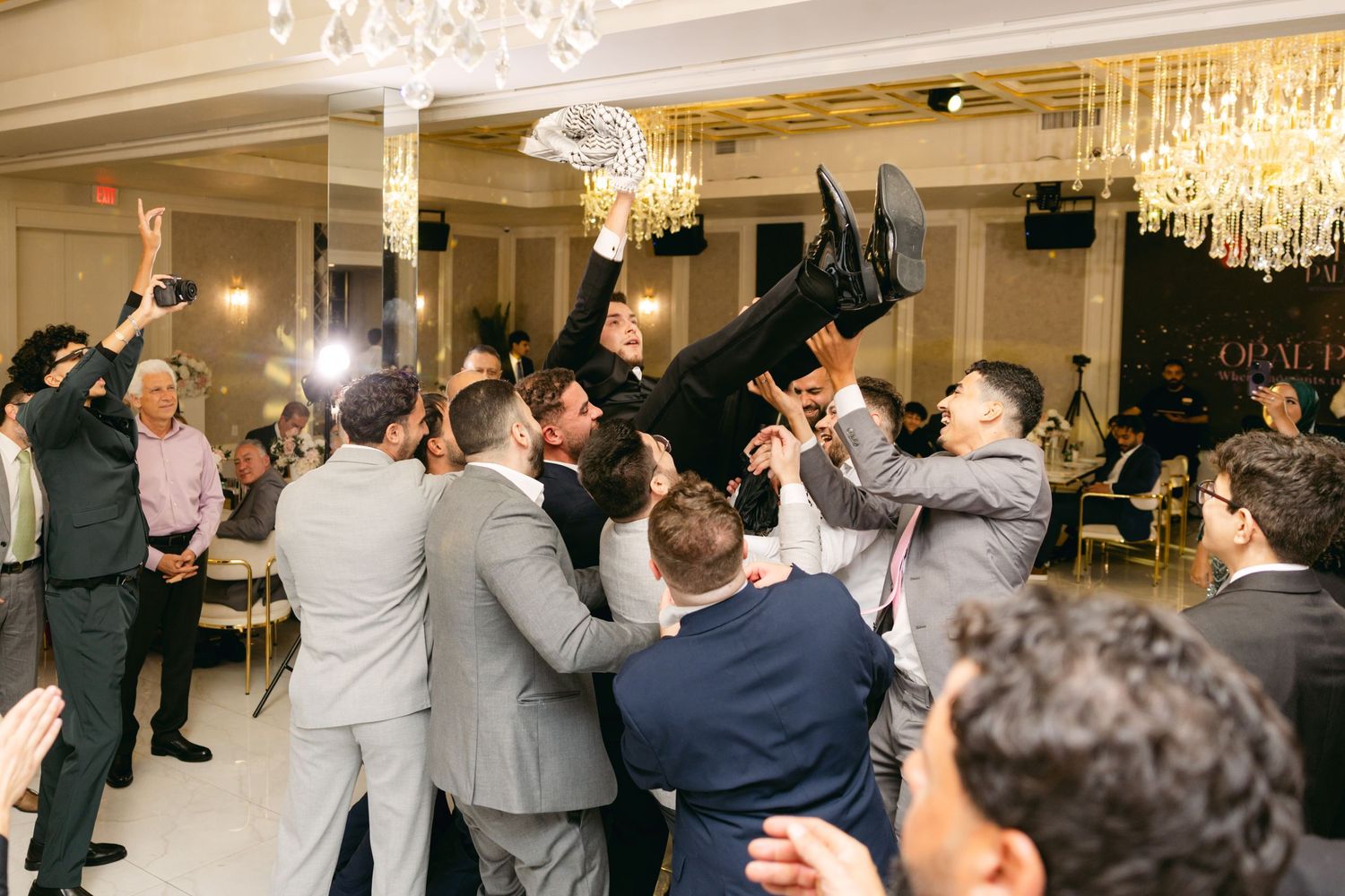 Wedding guests lift someone in celebration during a joyous moment at an elegant reception.
