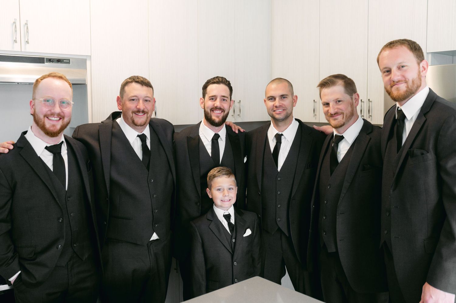 Wedding party of groomsmen in black suits posing with young ring bearer.