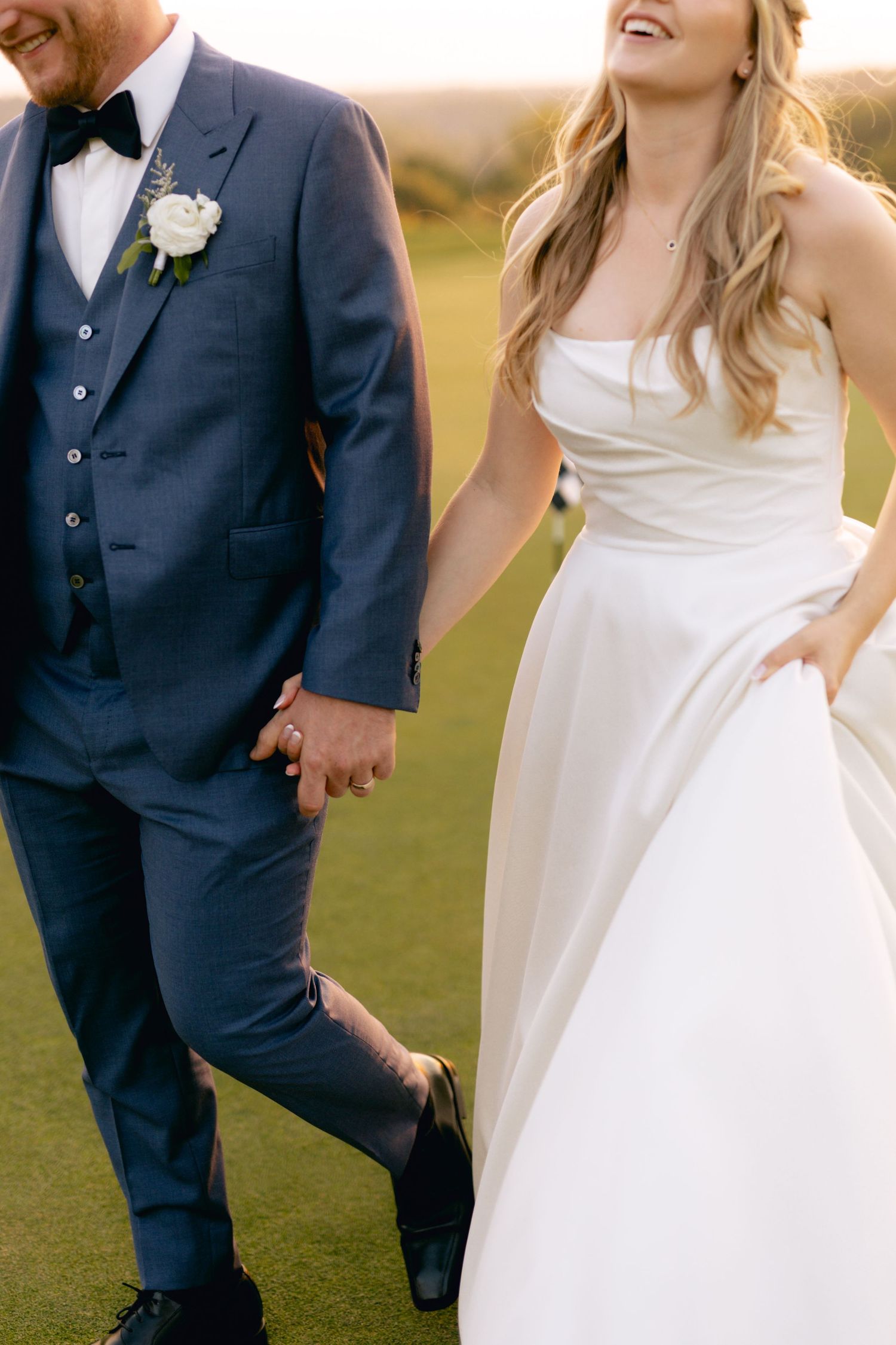 Joyful wedding couple shares candid moments on golf course during sunset.