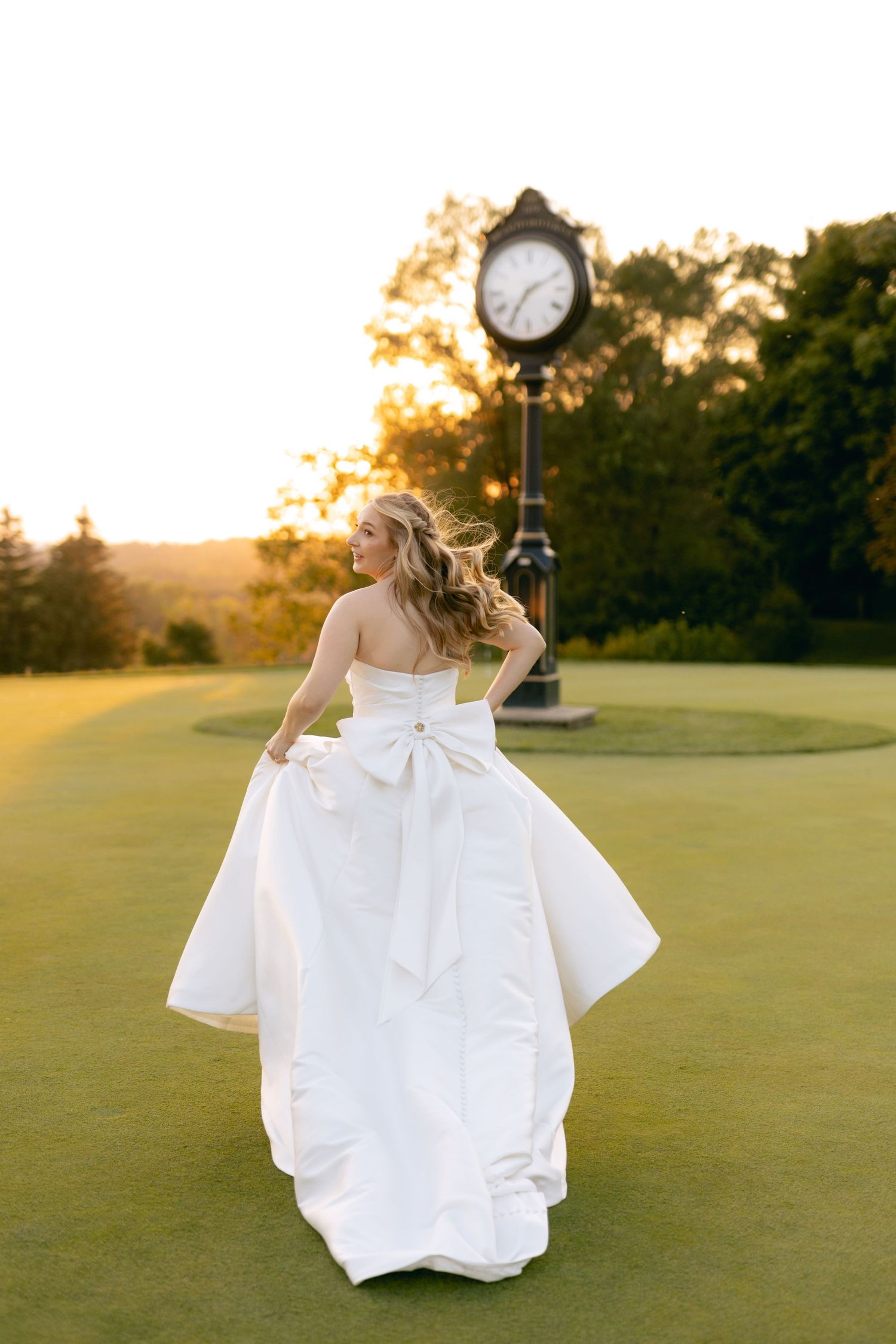 Flowing white wedding dress twirls against sunset backdrop on manicured golf course.