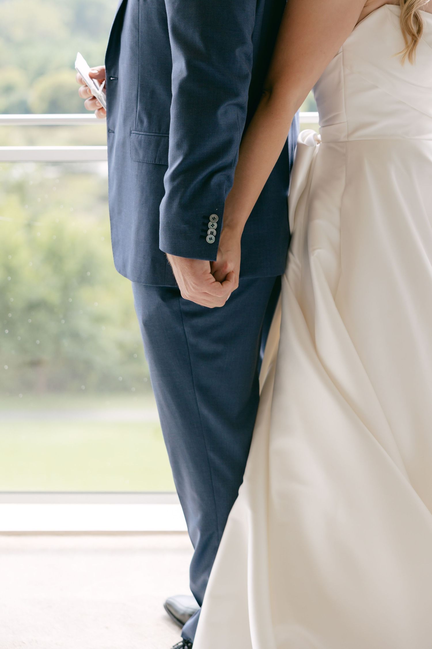 Detail shot of bride in white dress and groom in navy suit standing close together.