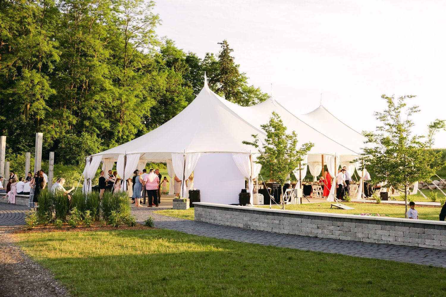White wedding tents set up on a grassy field with guests mingling in the background.