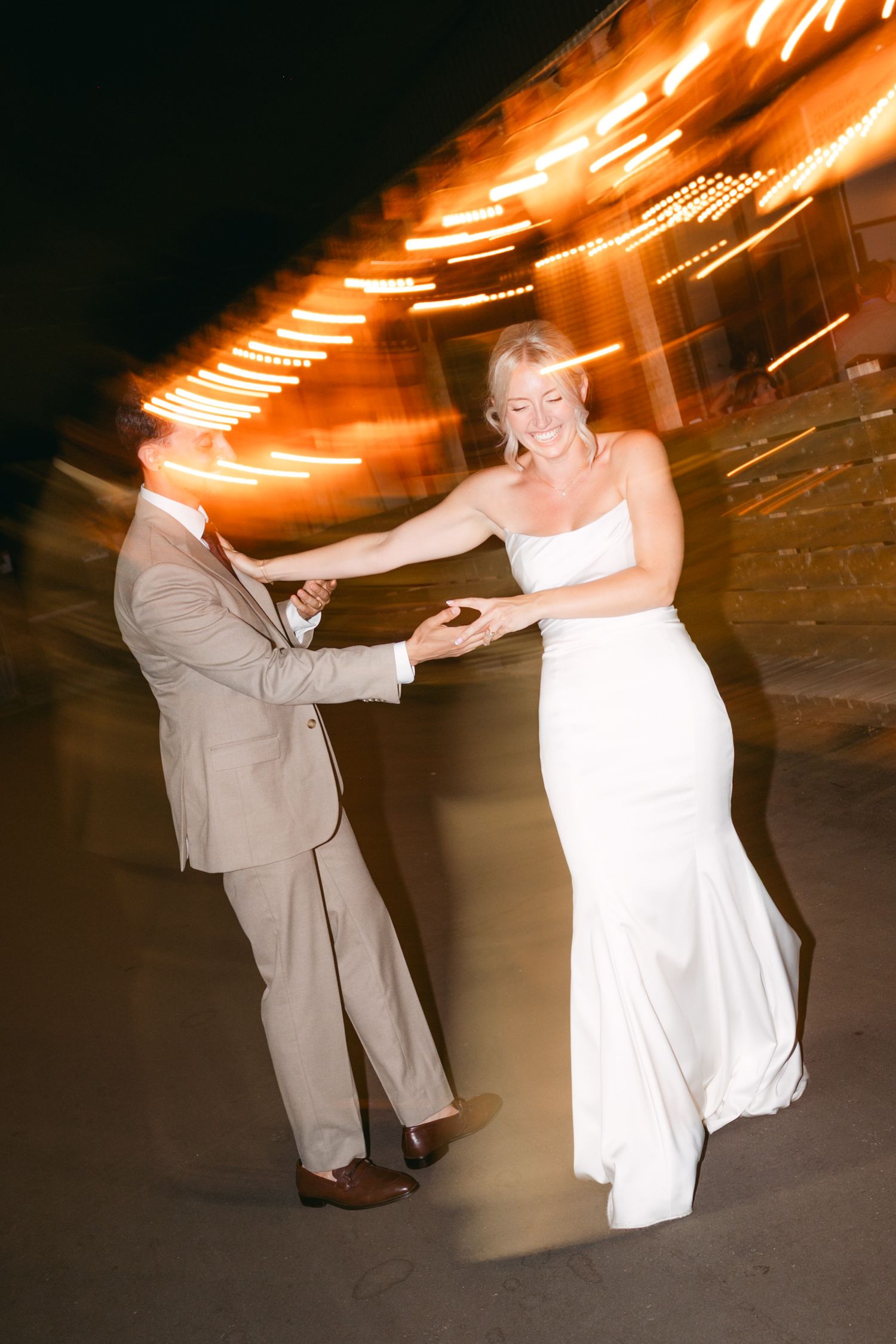 Couple dancing with motion blur and string lights creating artistic streaks above.