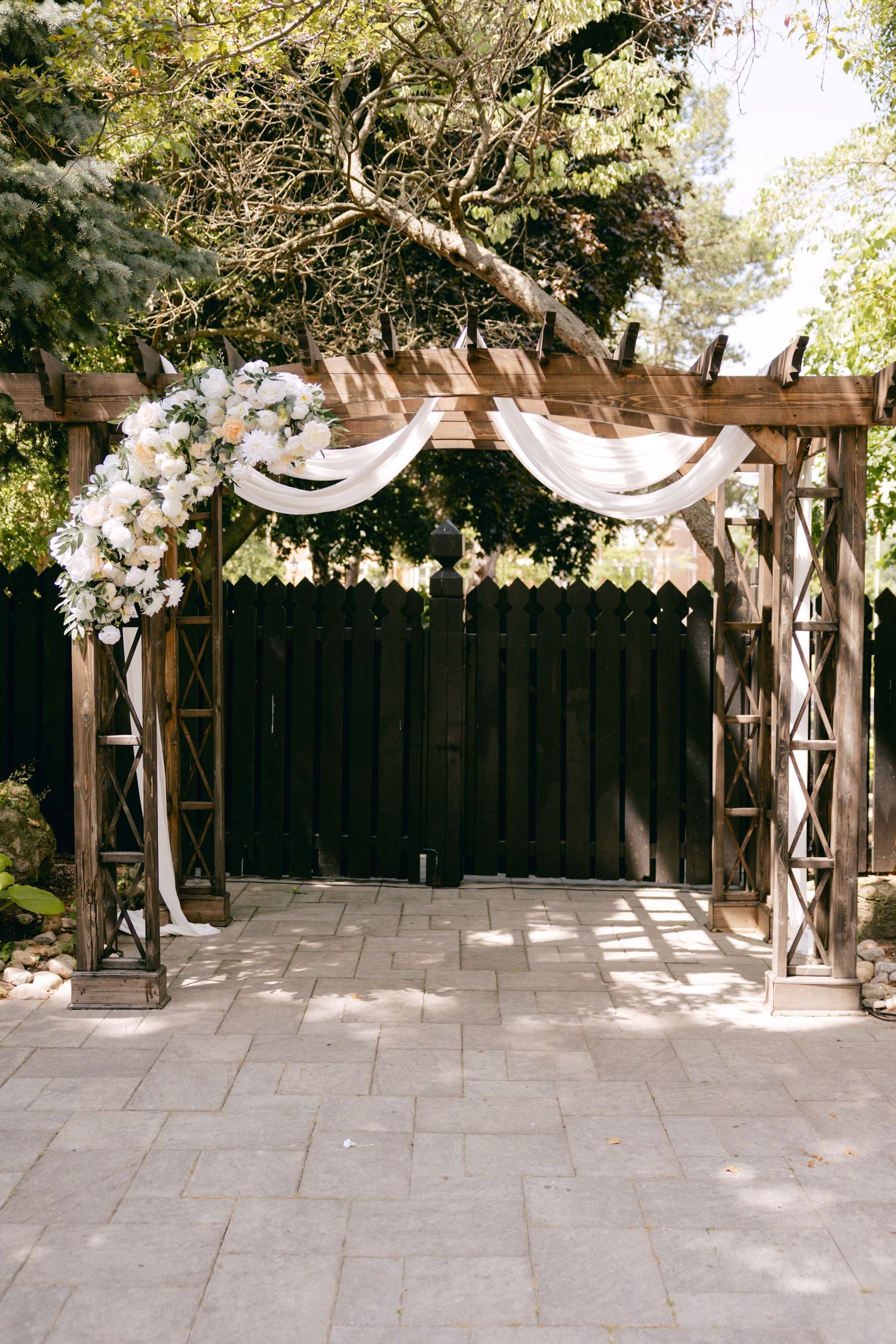 A wooden wedding arch decorated with white fabric draping and floral arrangements.