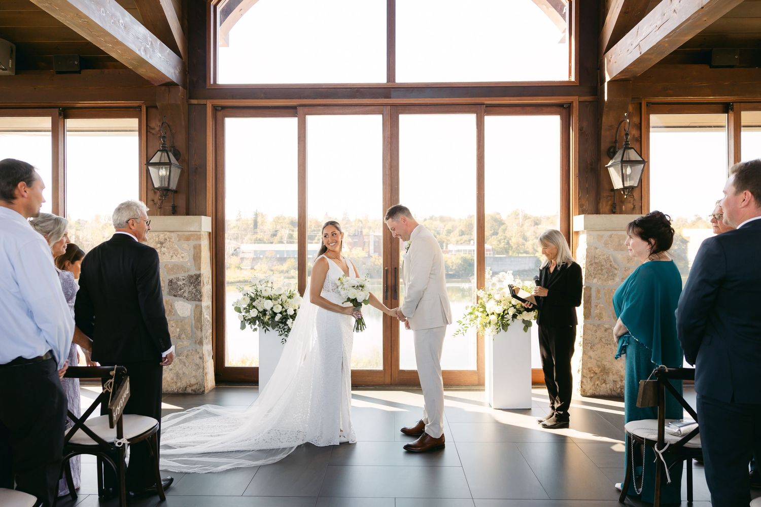 A wedding ceremony unfolds in front of floor-to-ceiling windows with elegant floral arrangements.