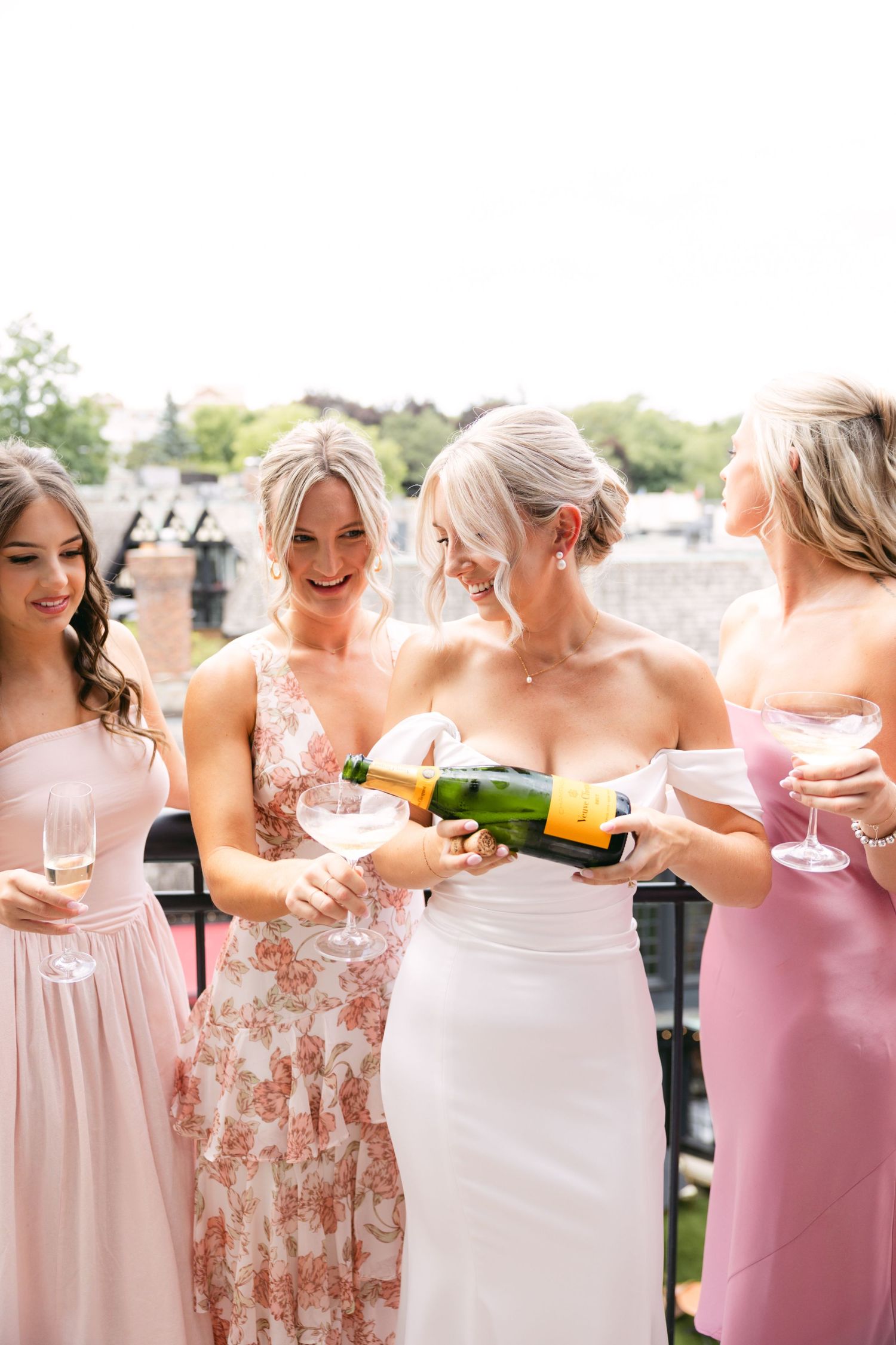 Bridal party in pink dresses pouring champagne during outdoor celebration.