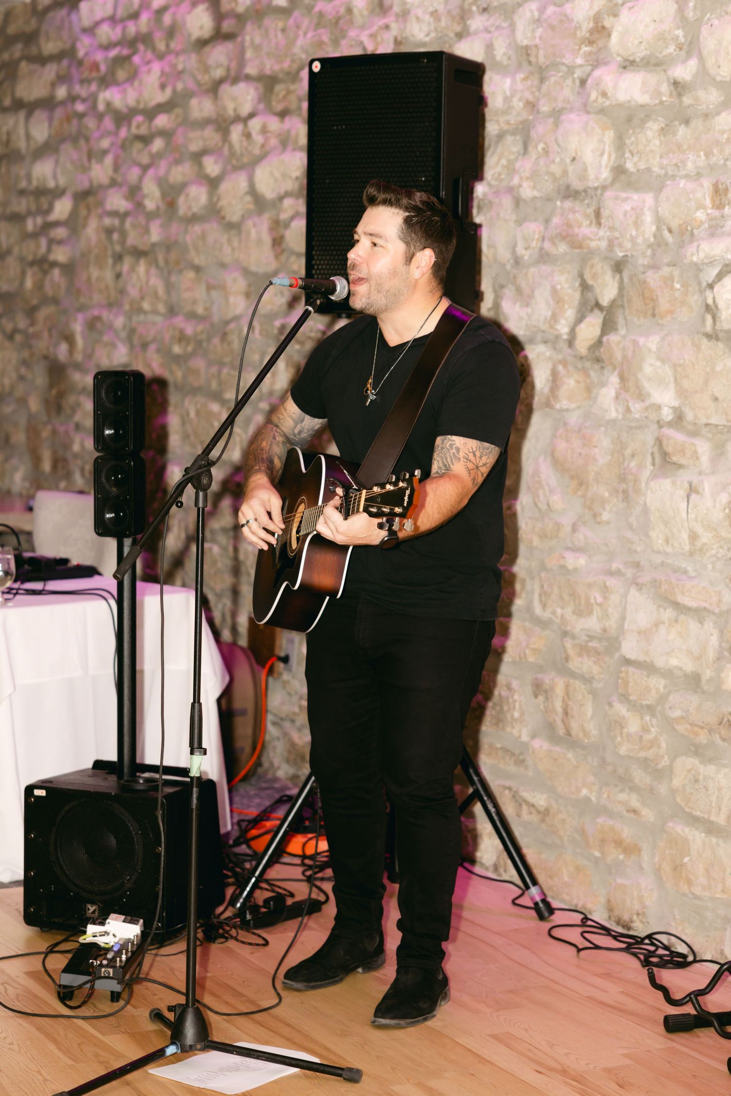 Musician performing with acoustic guitar against stone wall backdrop at wedding reception.
