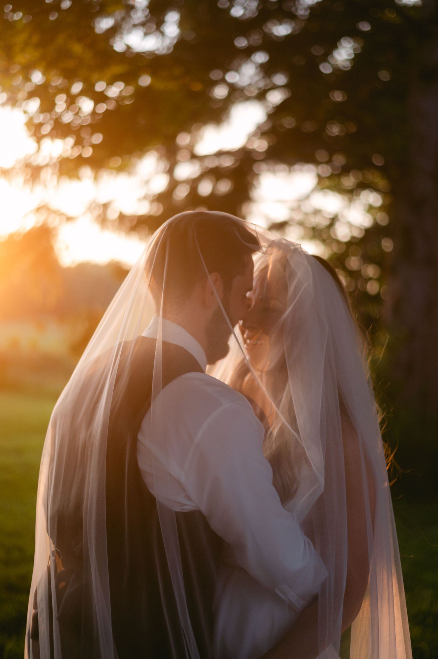 Romantic sunset wedding portrait with soft bokeh through trees.