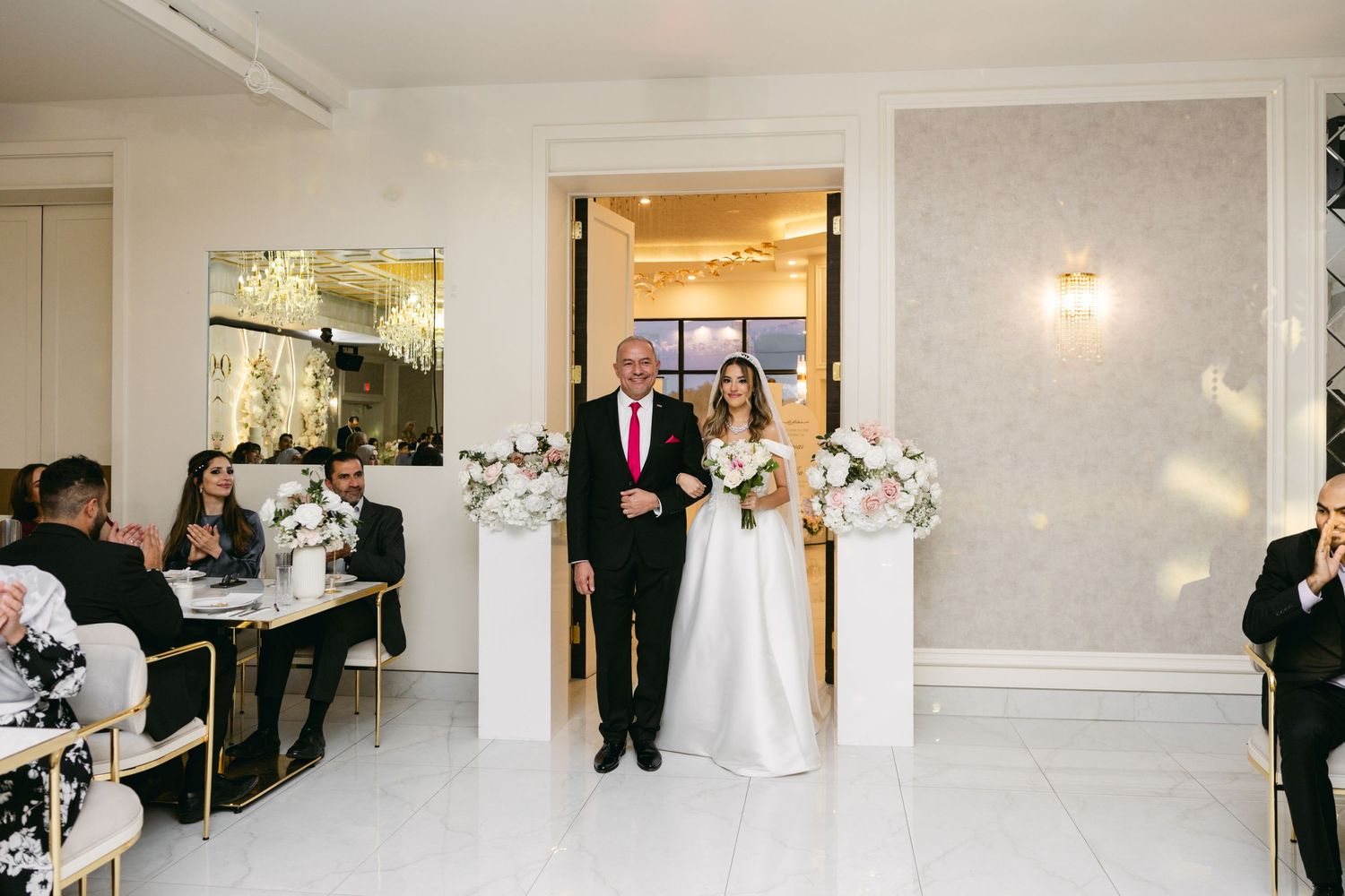 A traditional wedding entrance in an elegant white venue with crystal chandeliers.