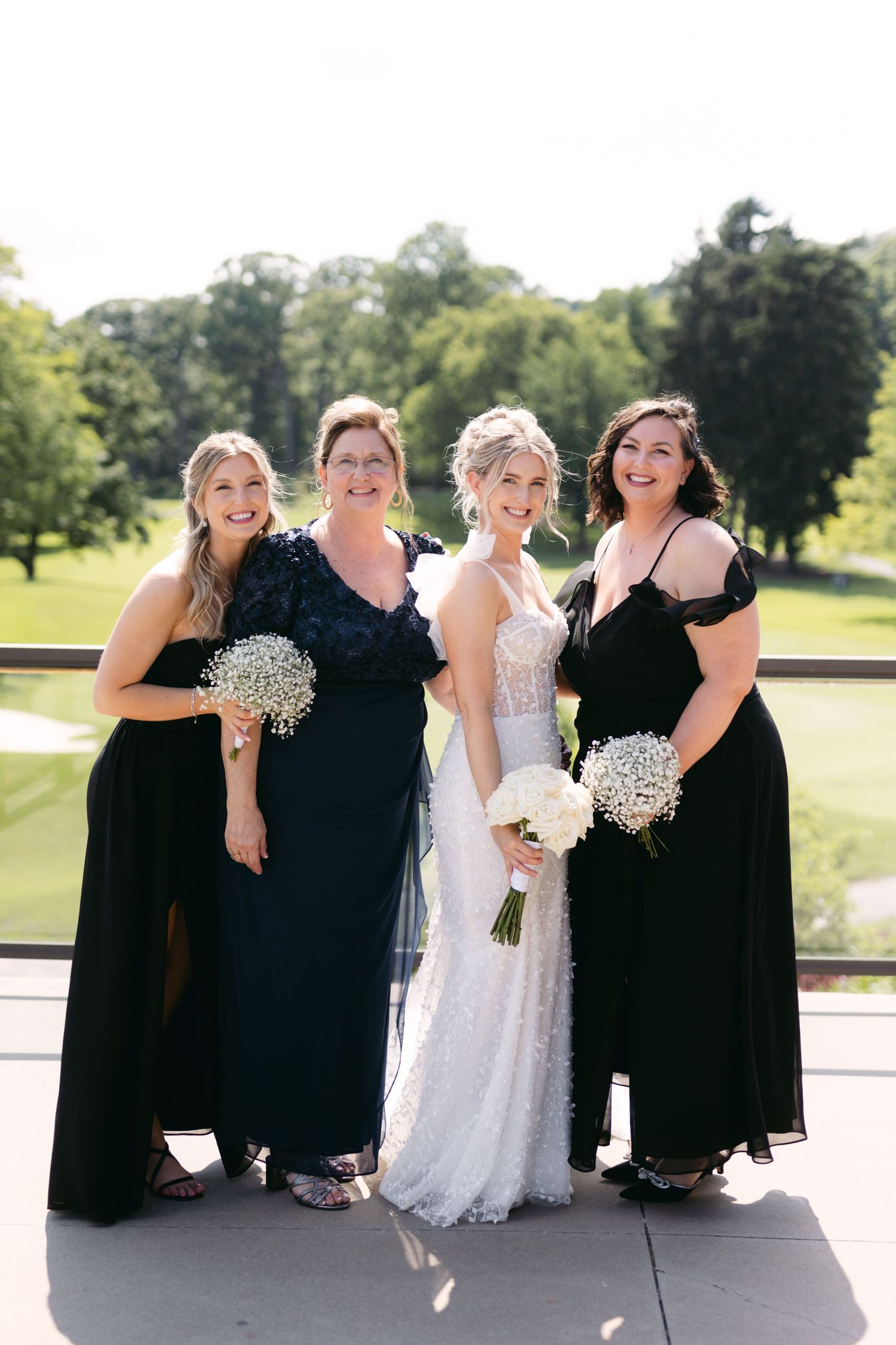 Bridal party in black dresses gather around the bride in white for casual group photos.