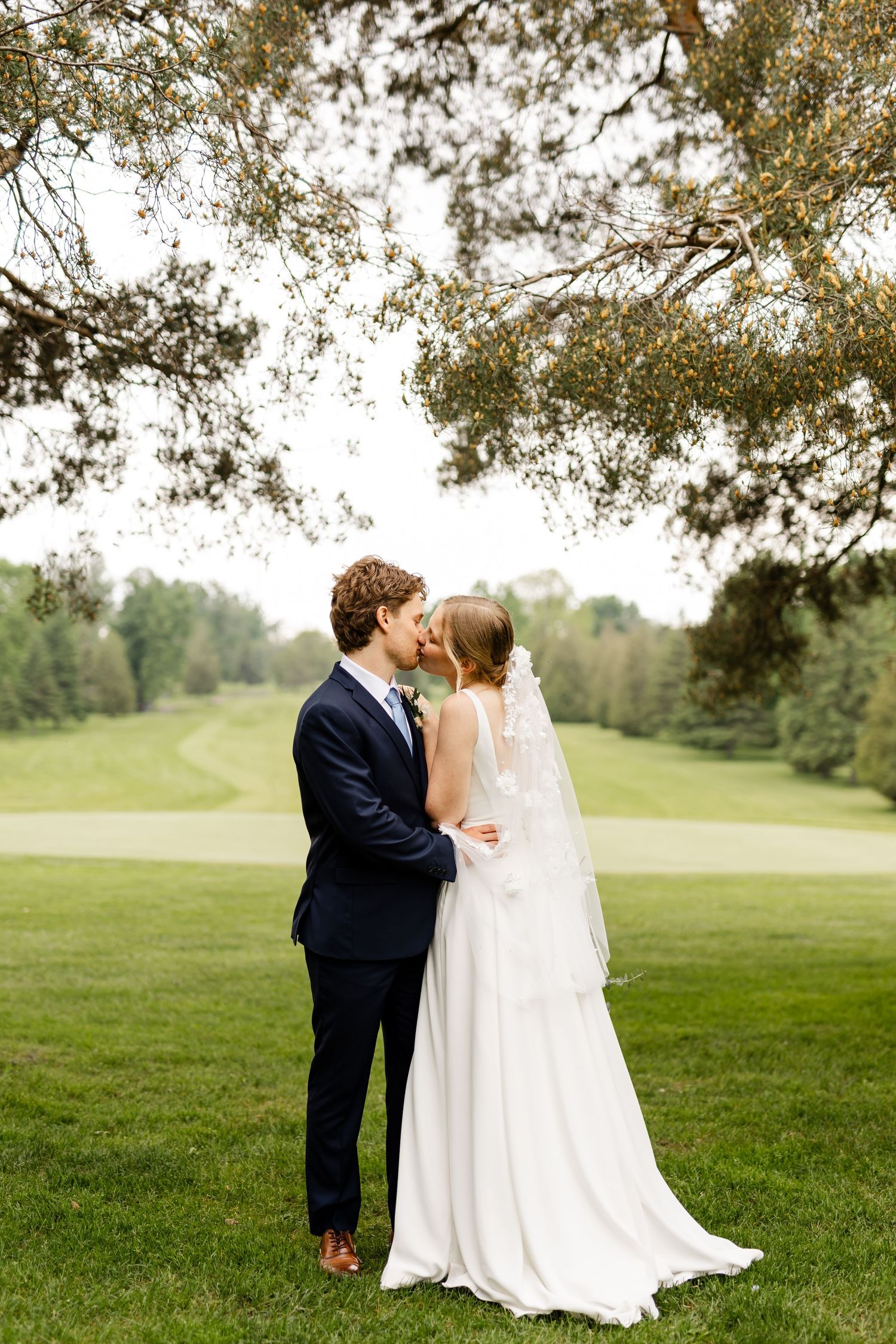 Romantic wedding portraits captured under tree branches on a golf course at sunset.