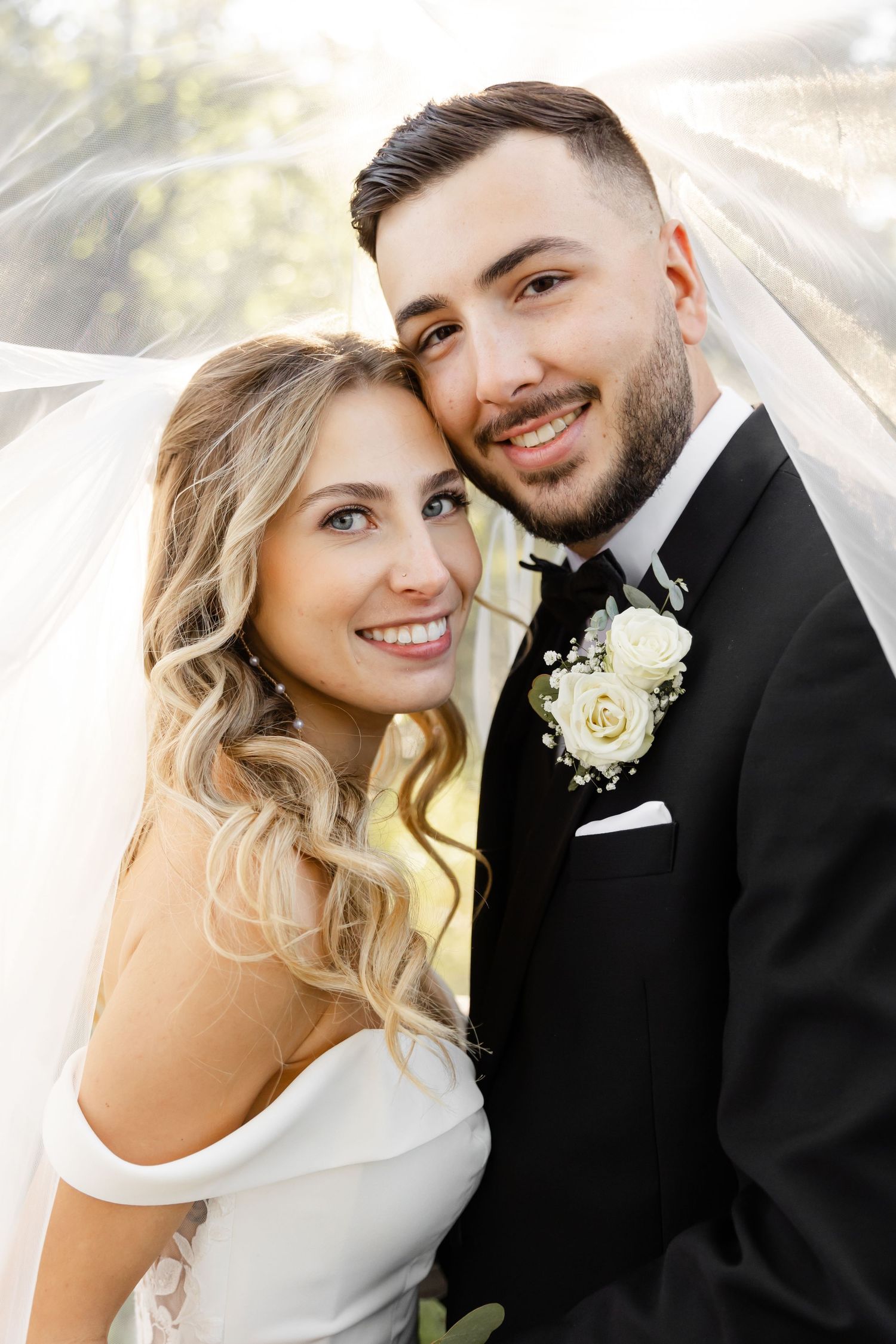 Romantic wedding portrait under flowing veil with soft natural lighting.
