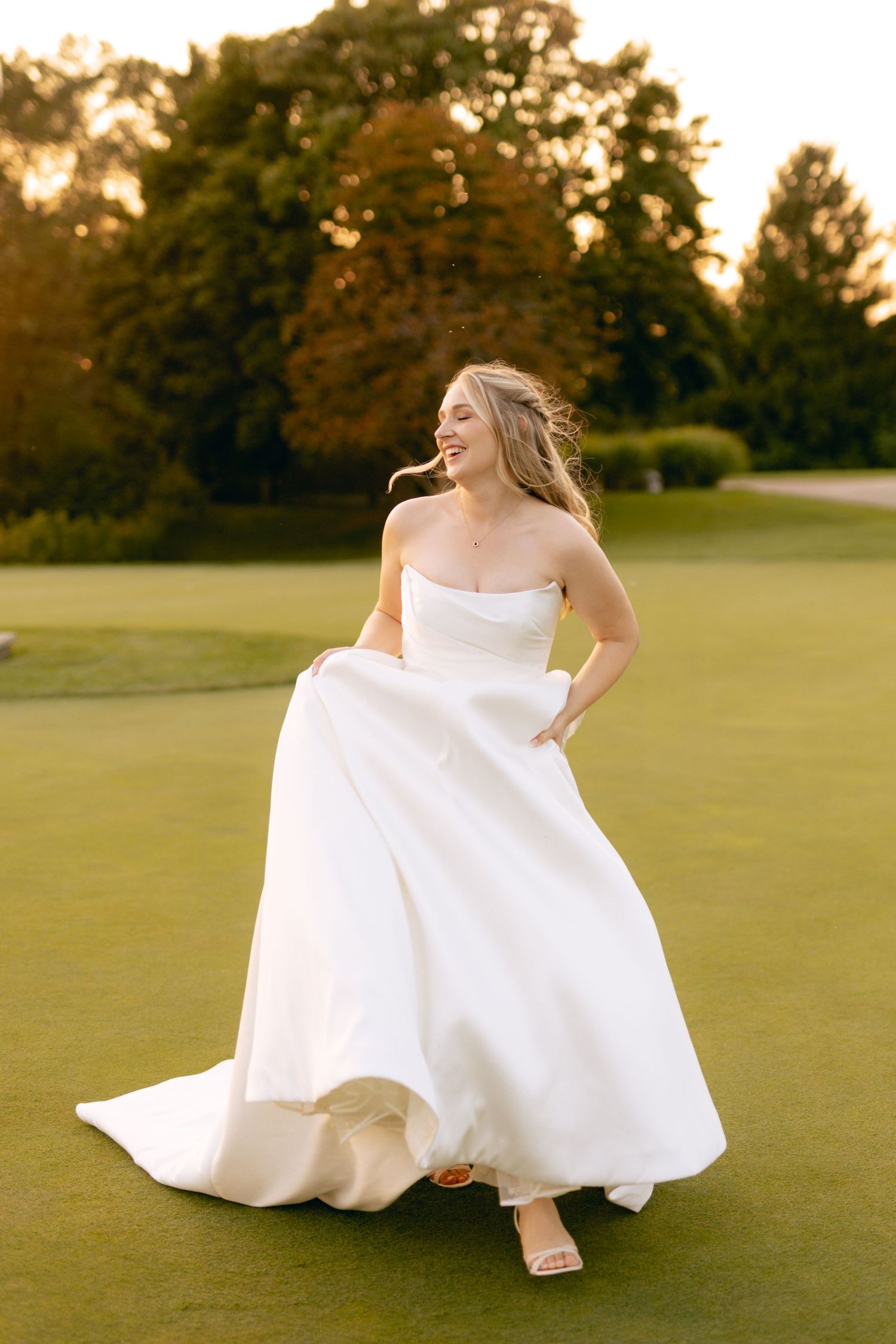 Bride twirls her dress playfully on golf course during sunset photo session.