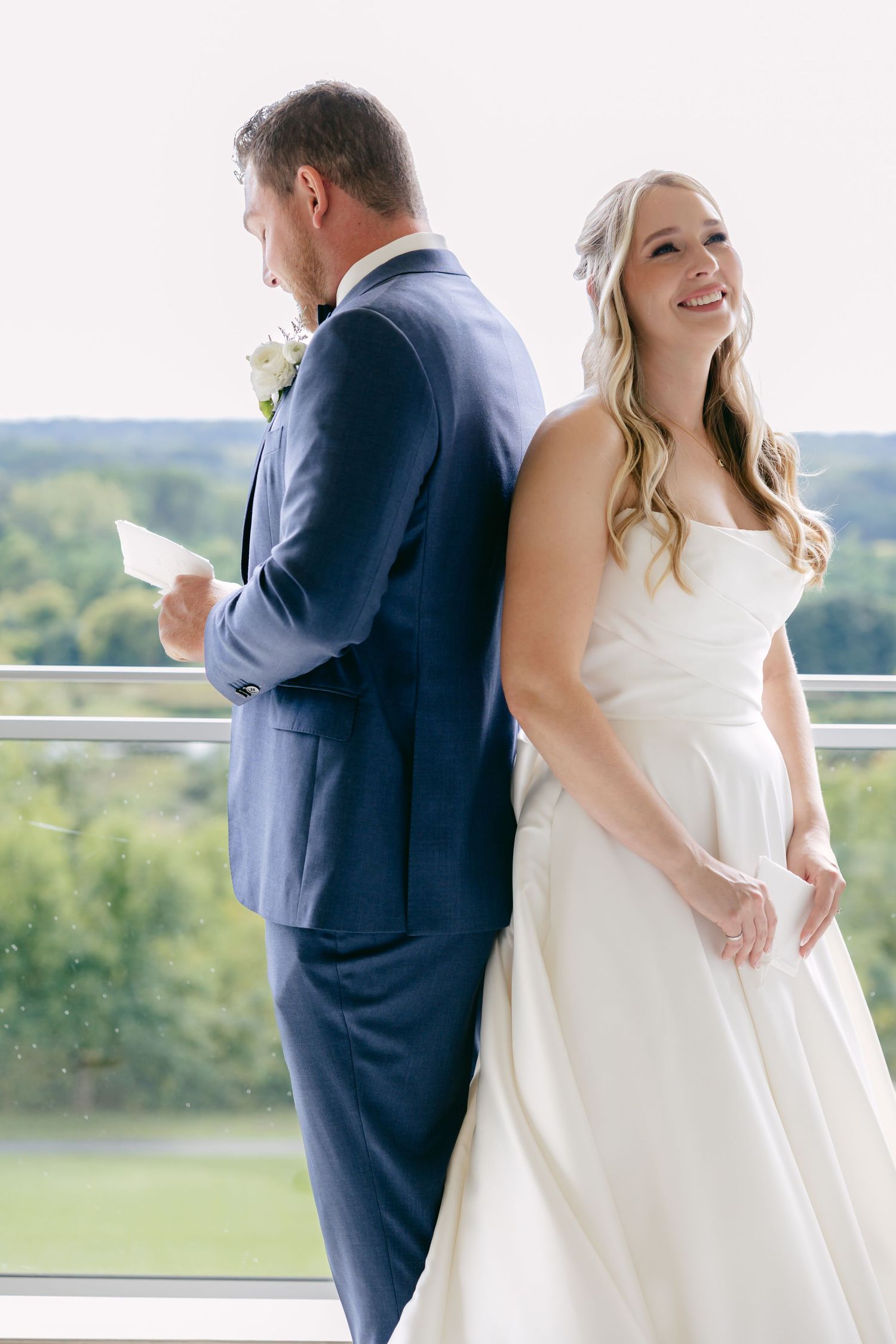 Wedding couple stands back to back on balcony while reading letters.