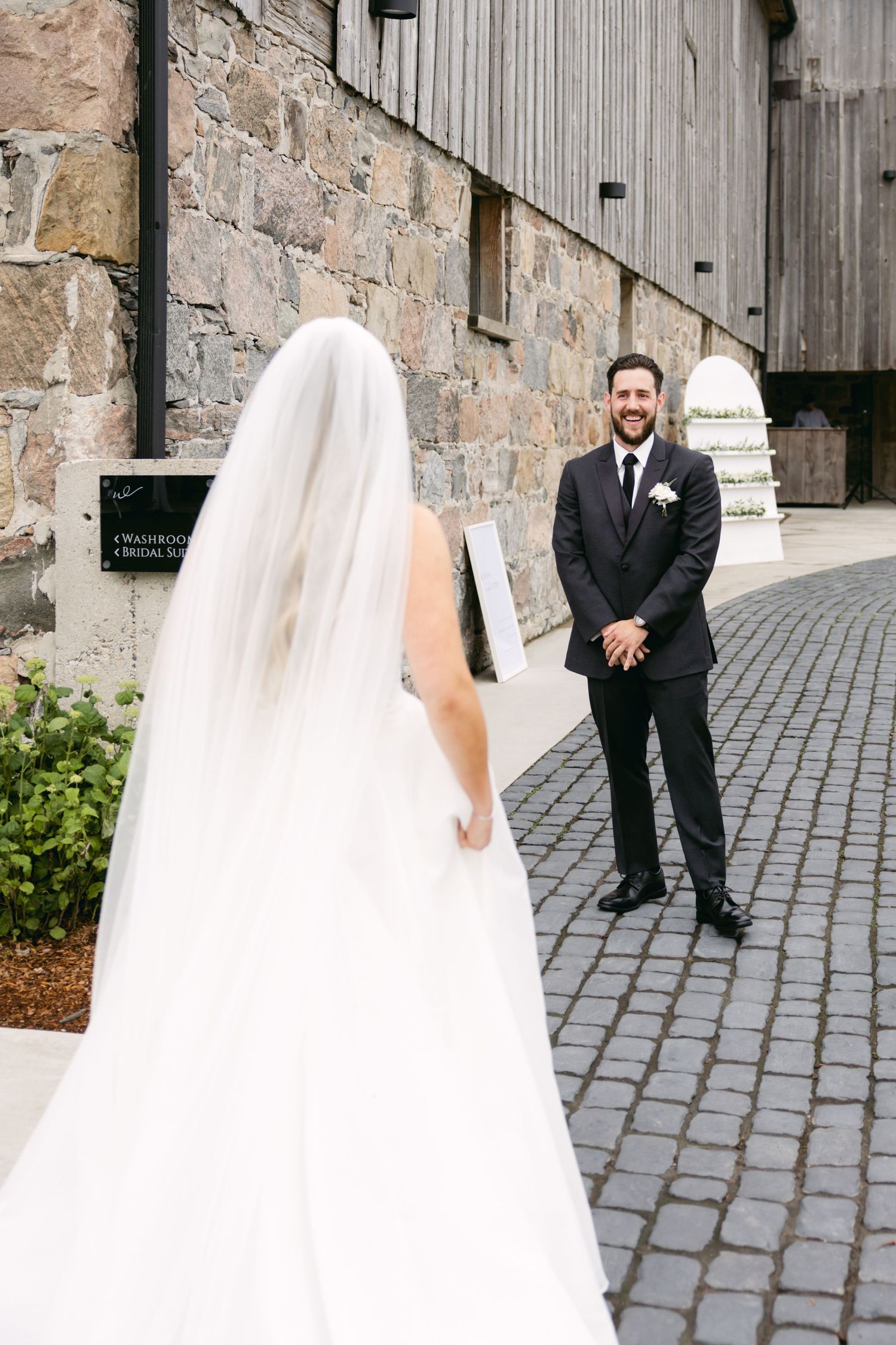 First look wedding moment outside rustic stone and wood barn.