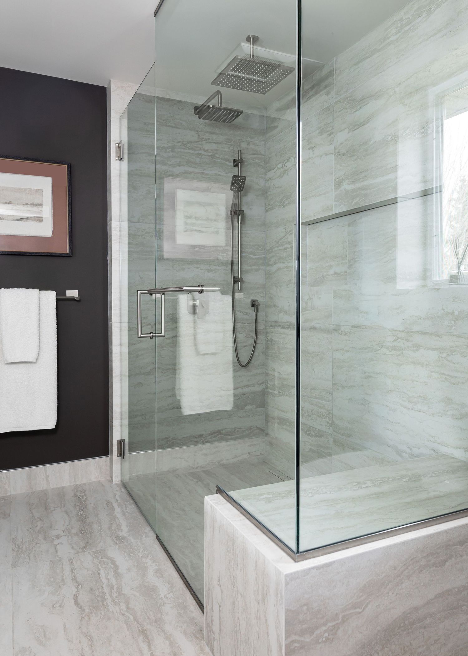 Spacious glass-enclosed shower featuring marble tile walls and modern rainfall showerhead fixtures.