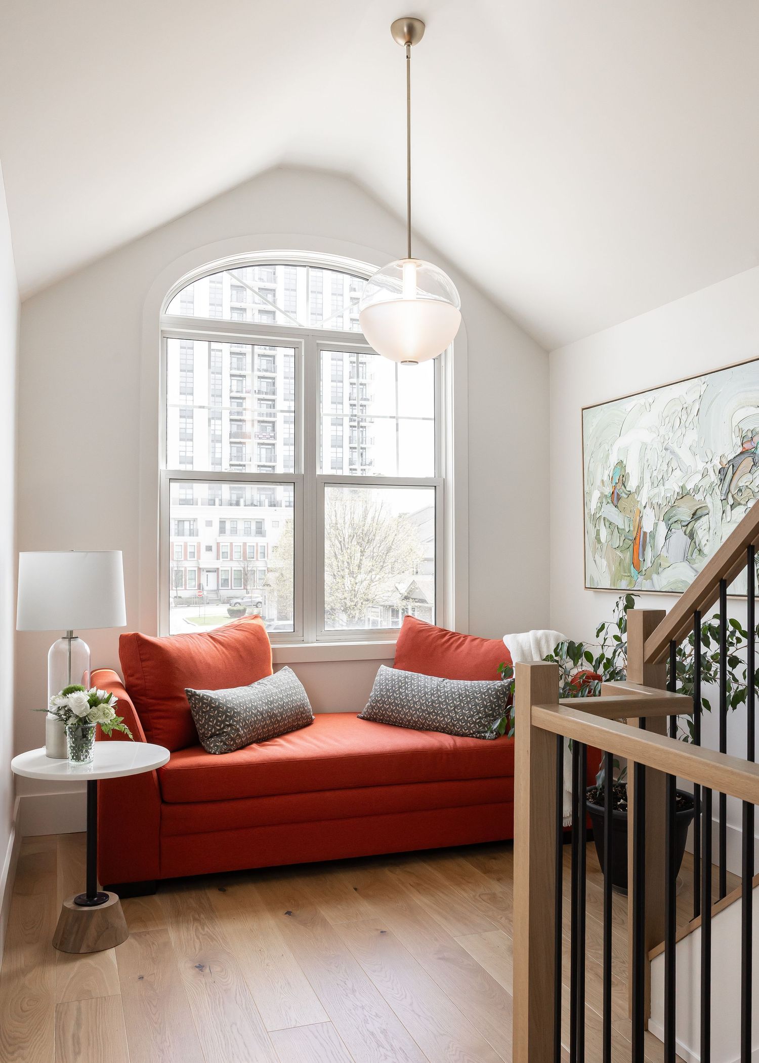 Loft space with arched windows, coral daybed, and wooden stair railing overlooking living area.