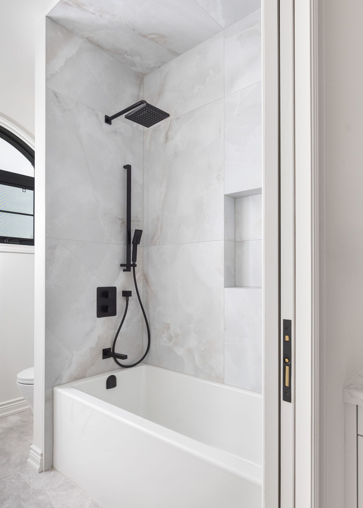 Modern white bathroom with black fixtures featuring built-in tub and rainfall showerhead.