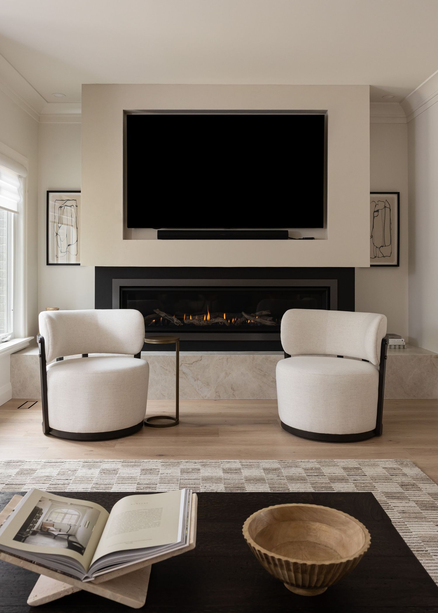 Minimalist living room with curved white seating, geometric rug, and horizontal fireplace feature wall.