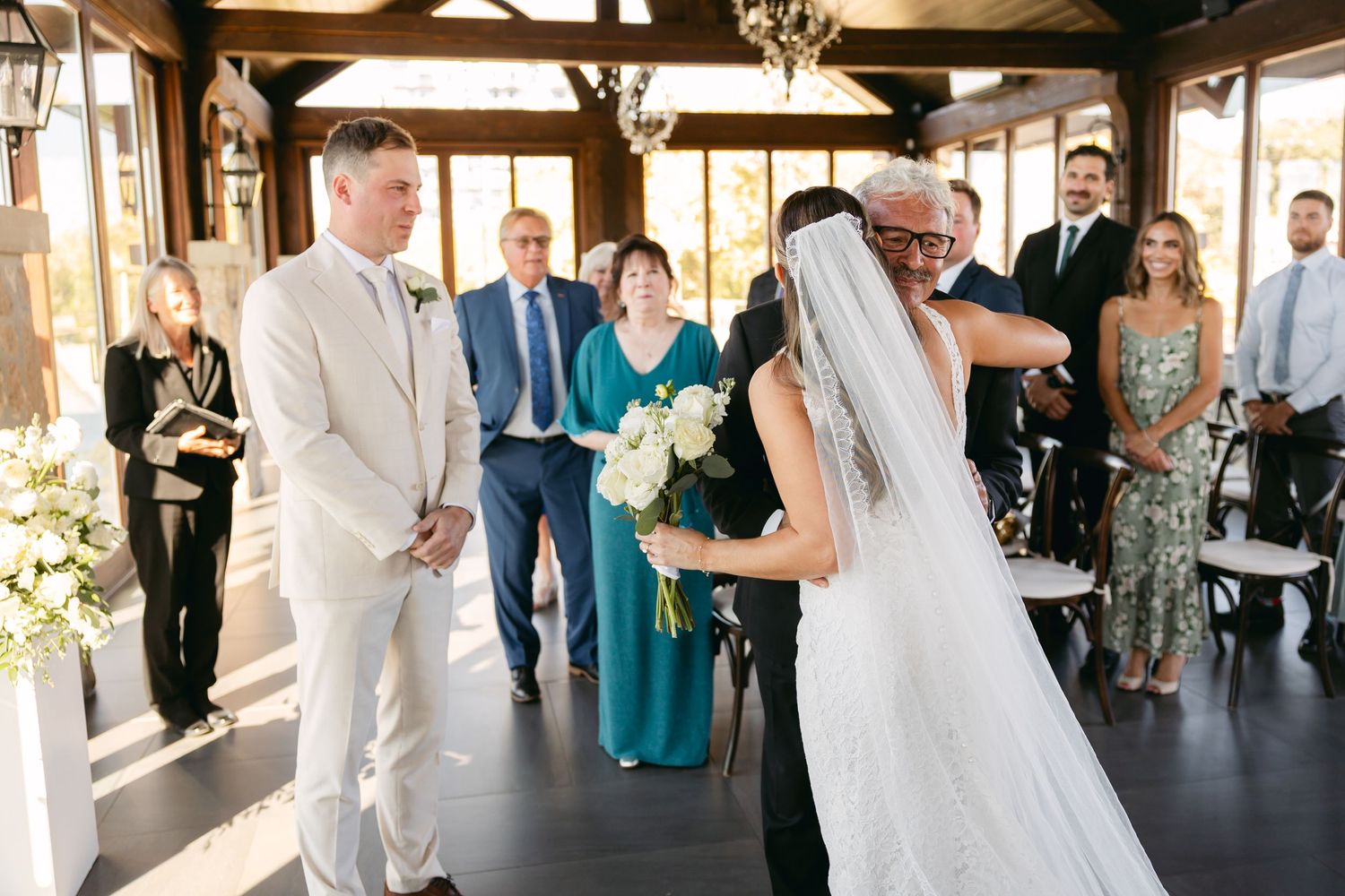 Wedding guests watch as a ceremony unfolds in an elegant venue with wooden beams and natural light.