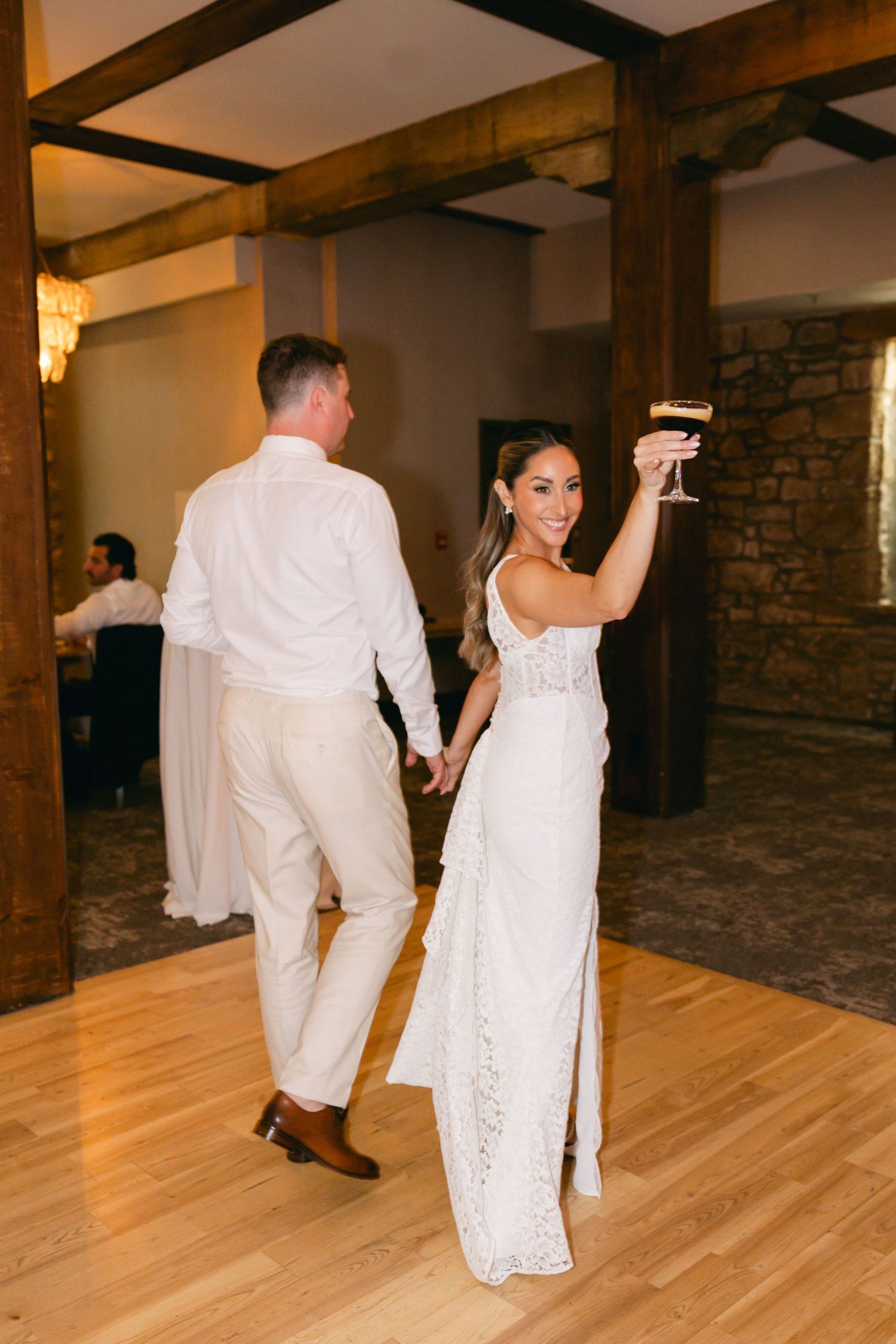 Couples dancing on a hardwood floor at a wedding reception with rustic stone walls and wooden beams.