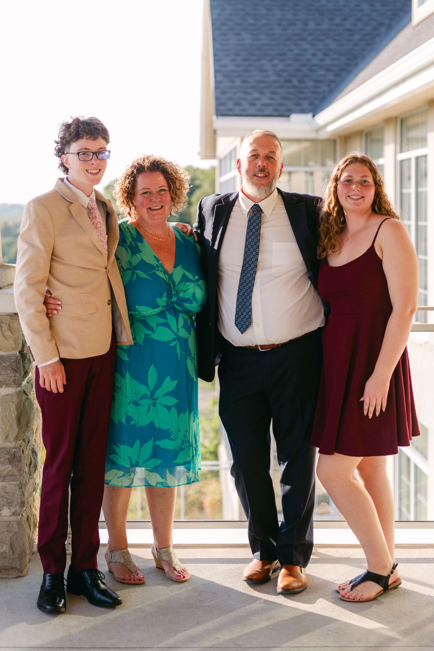 Four people in formal attire smile while posing together on a covered porch.