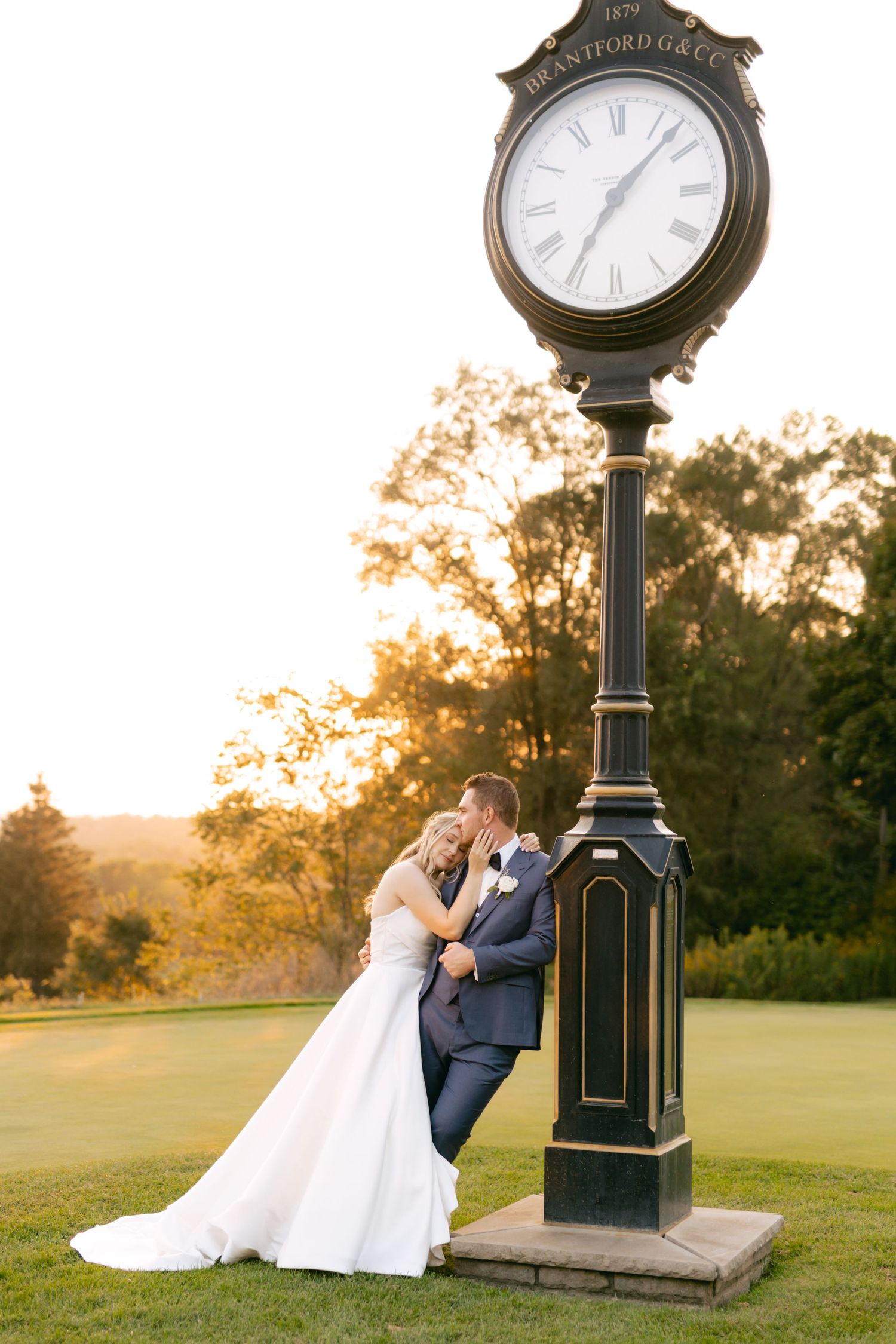 Wedding portraits captured at sunset beside vintage clock post on rolling green landscape.