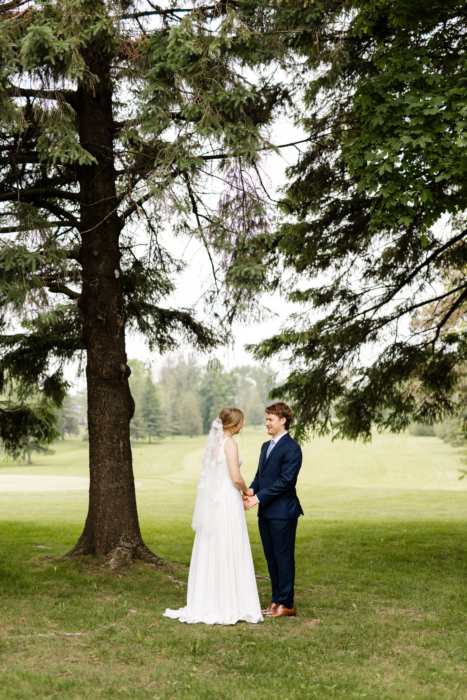 A romantic wedding portrait beneath towering pine trees on a misty green landscape.