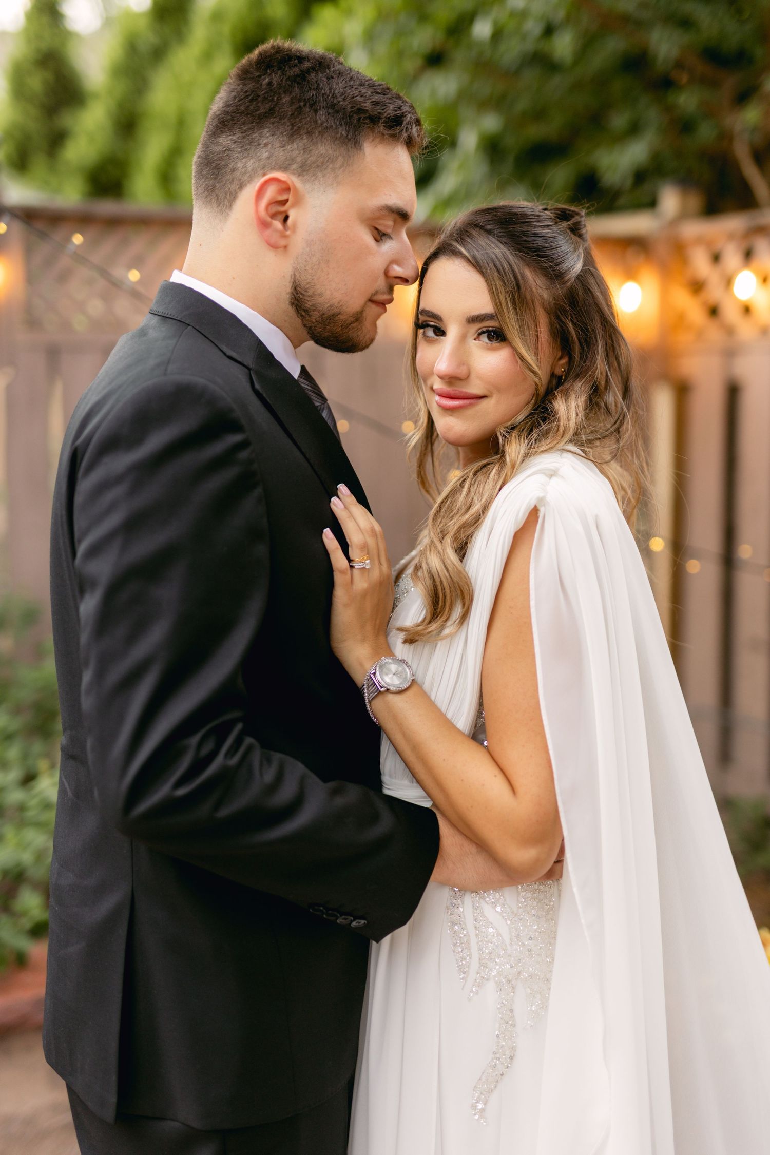 Intimate moment between newlyweds in outdoor garden setting with string lights.