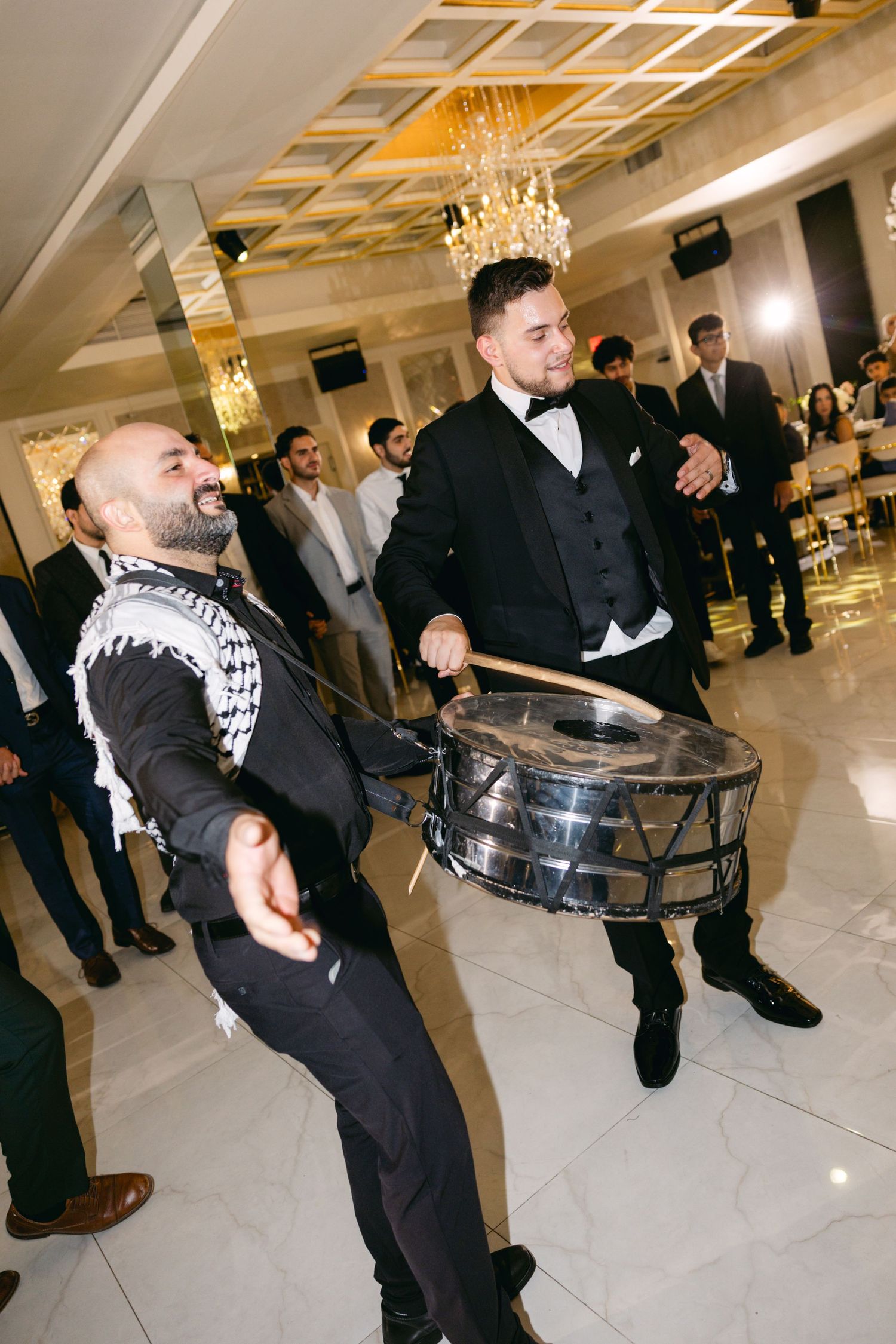 Guests playing drums during wedding reception entertainment in an elegant white venue.