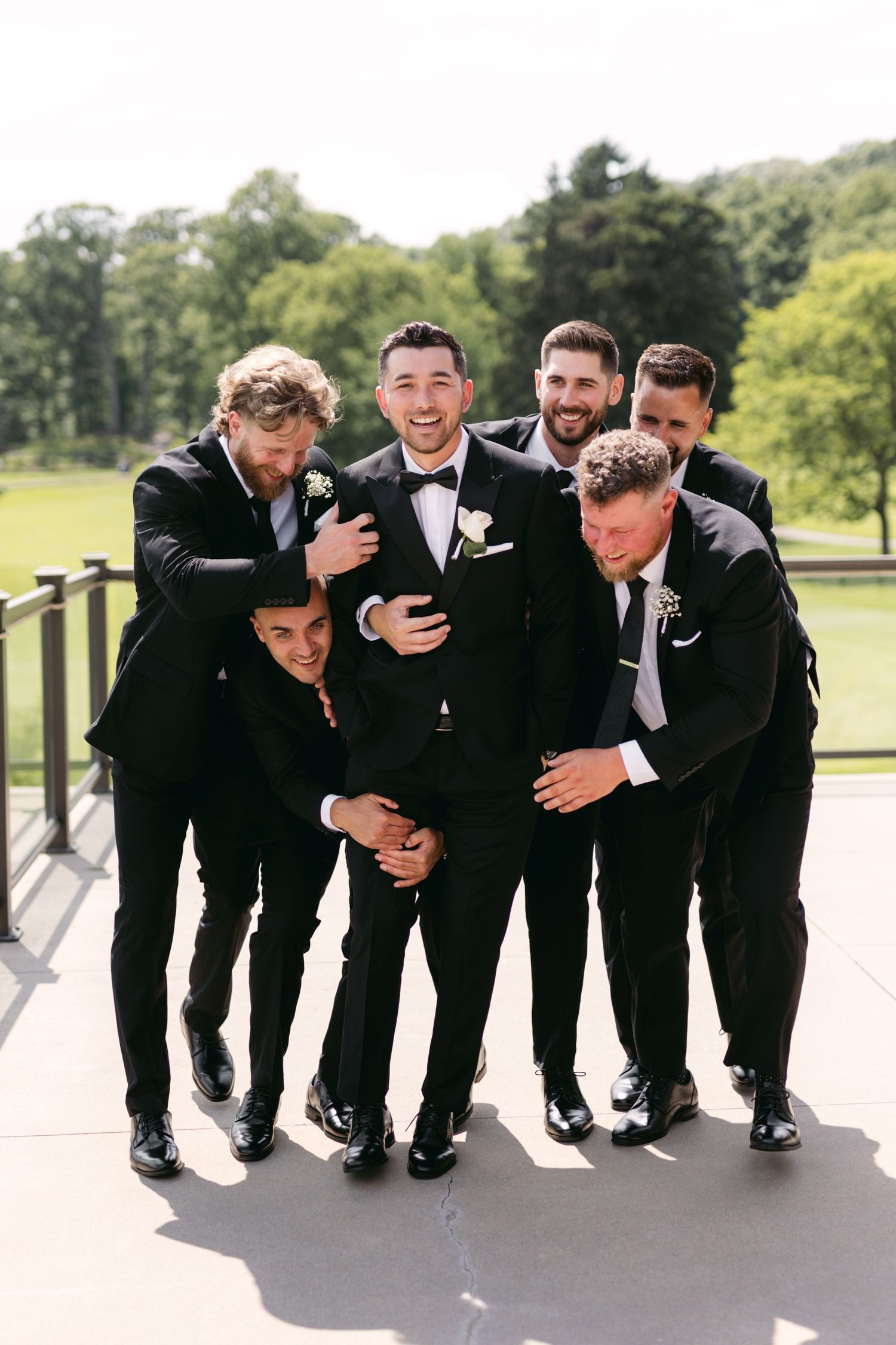 Groomsmen share a laugh while huddled together in formal attire.