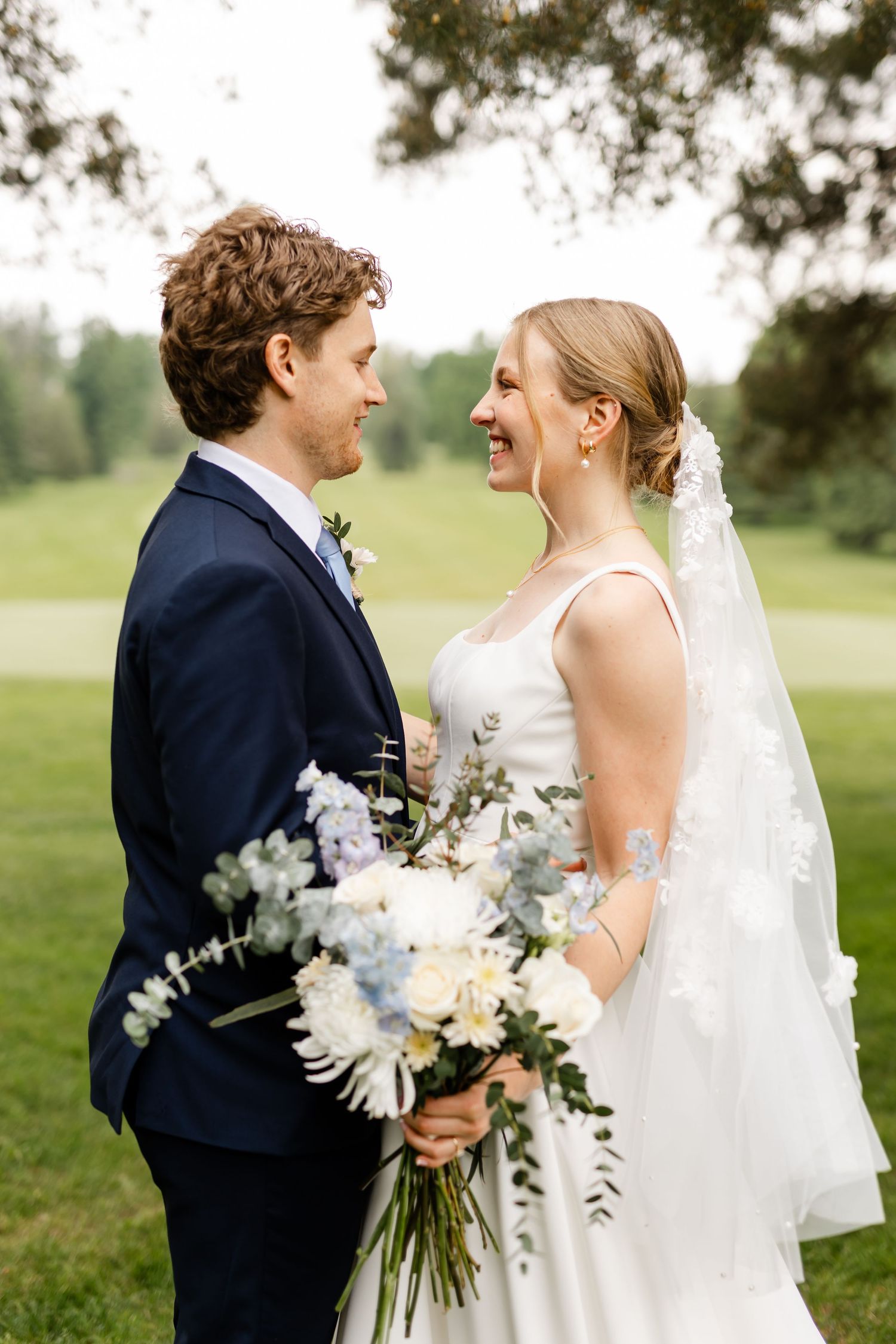 Newlyweds hold a beautiful white floral bouquet while sharing intimate moments outdoors.