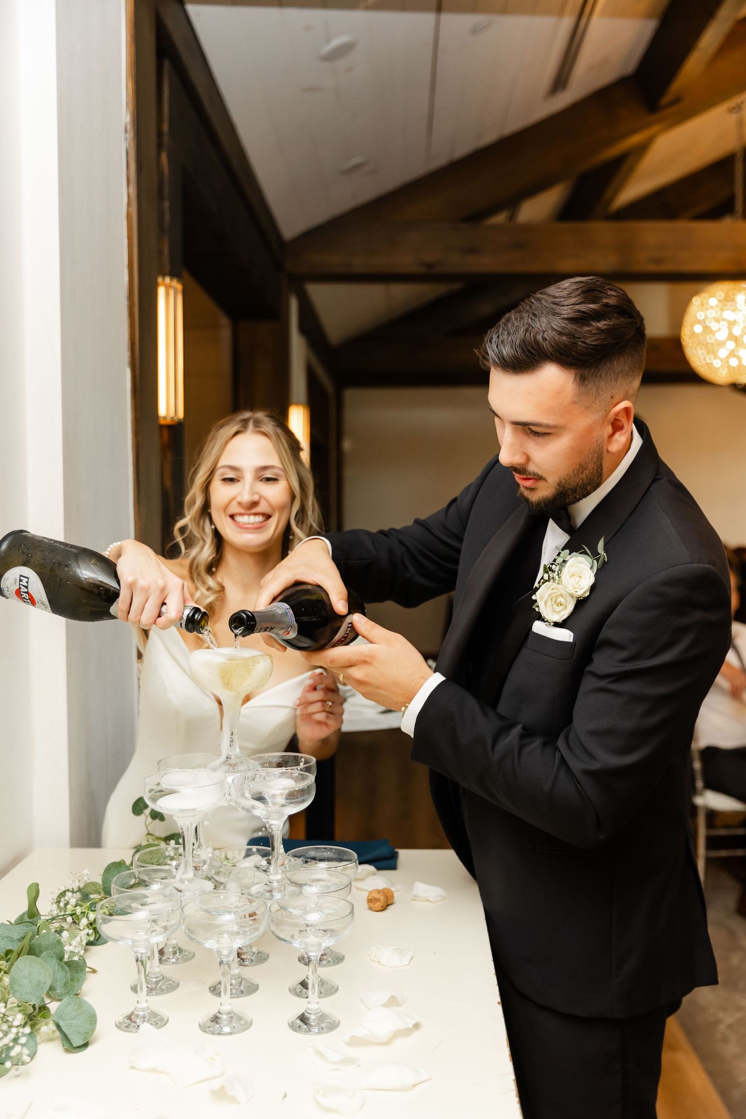 Wedding couple carefully pouring champagne into a glass tower display at their reception.