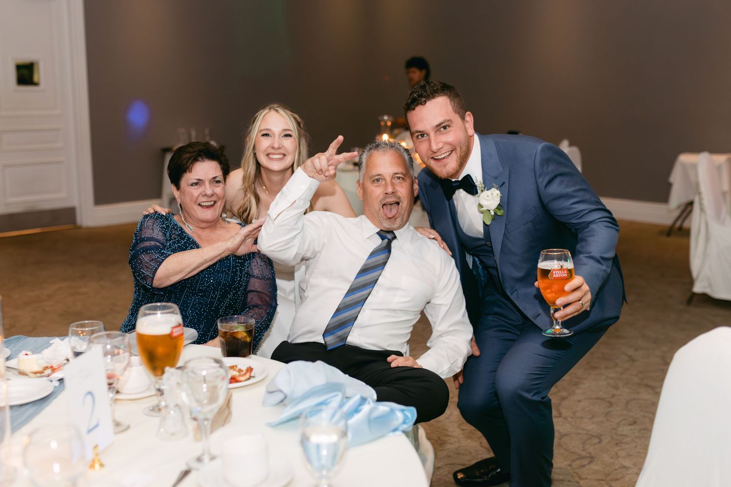 Wedding reception guests enjoying drinks and laughter at tables decorated with floral centerpieces.