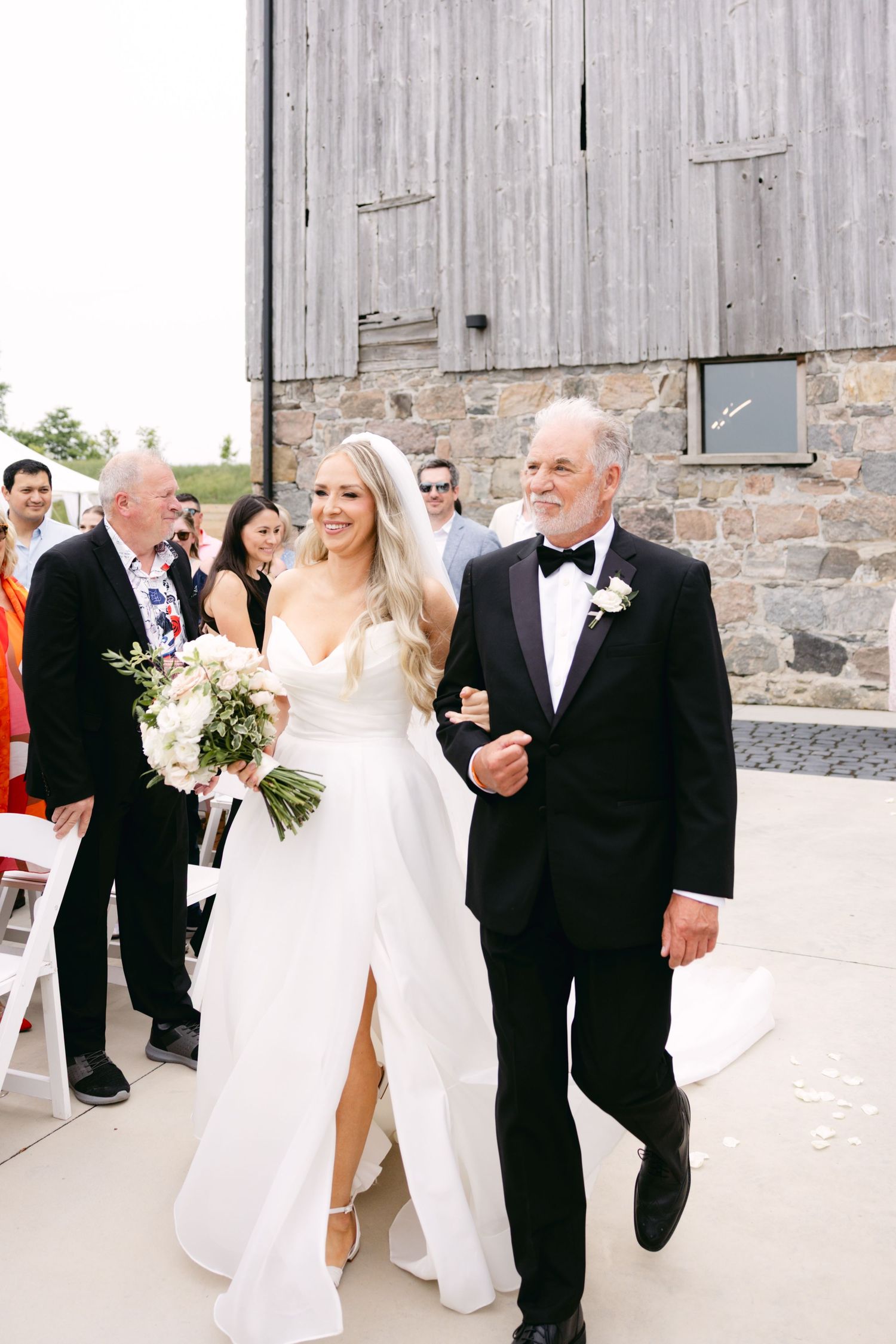 Wedding celebration with guests walking along rustic stone building exterior.