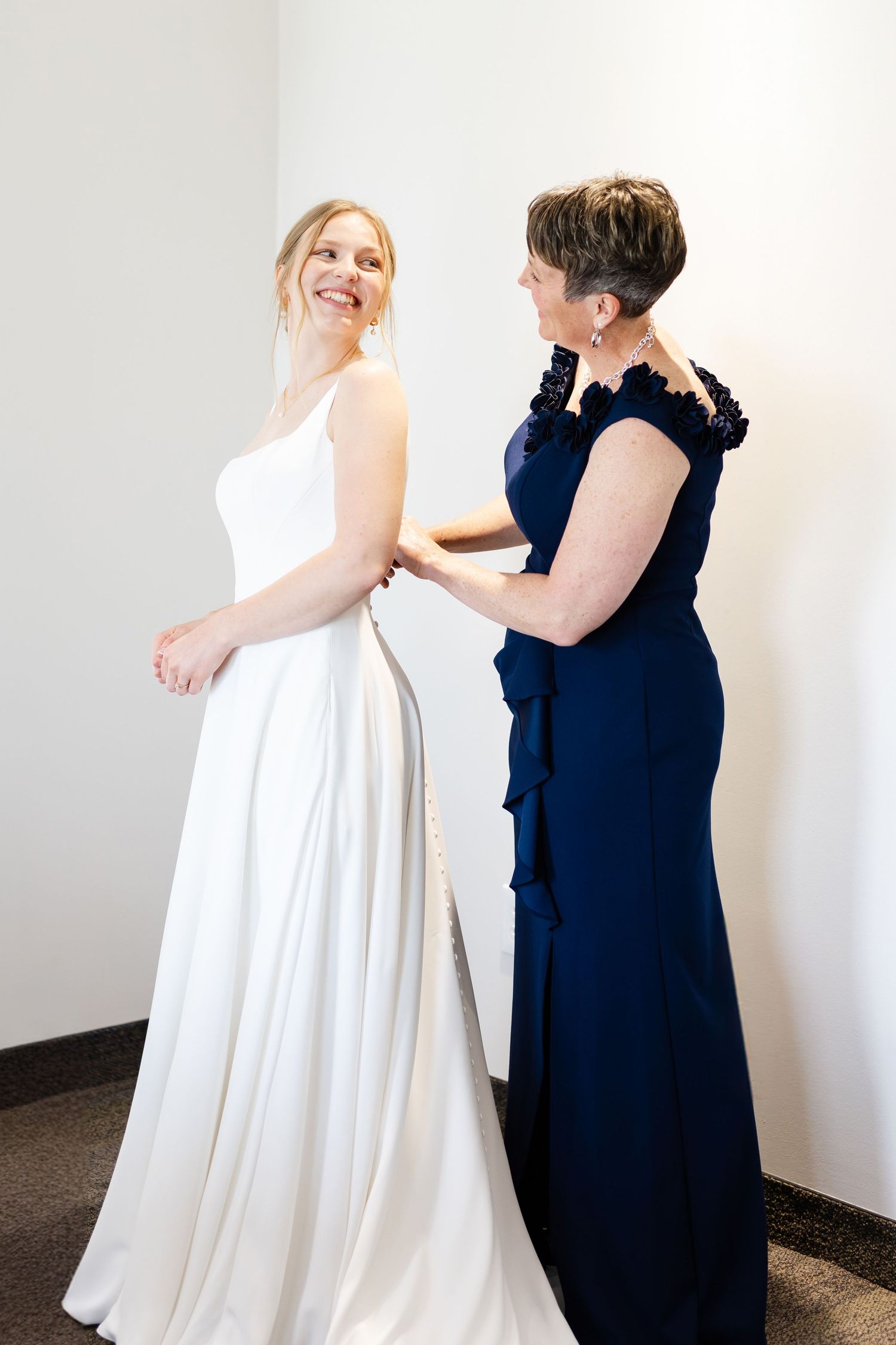 Wedding dress fitting scene with attendant helping bride with final adjustments.