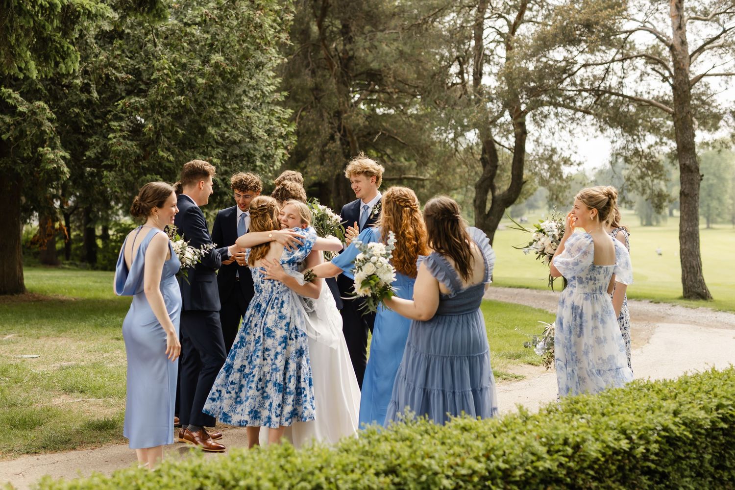 Wedding party in blue dresses gathers for celebratory moment on grassy lawn.