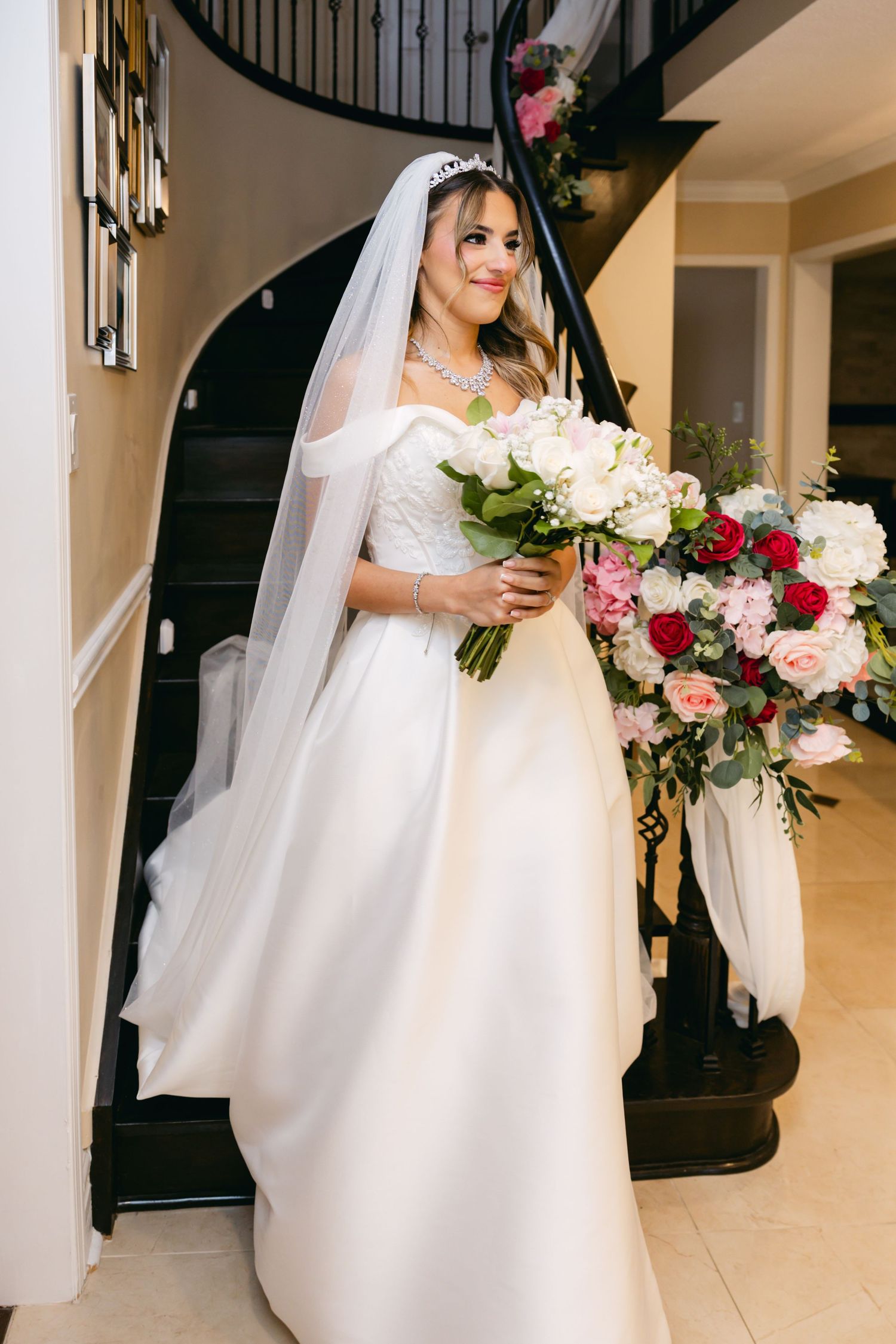Bride holding pink and white bouquet while standing near elegant staircase.
