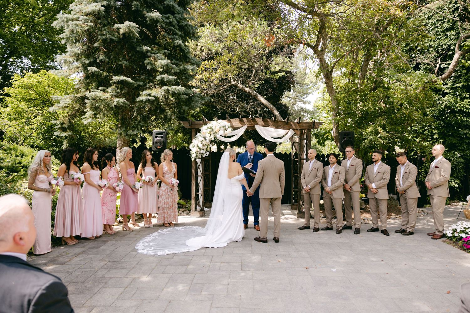 Wedding party poses for group photos on stone pathway surrounded by lush greenery.