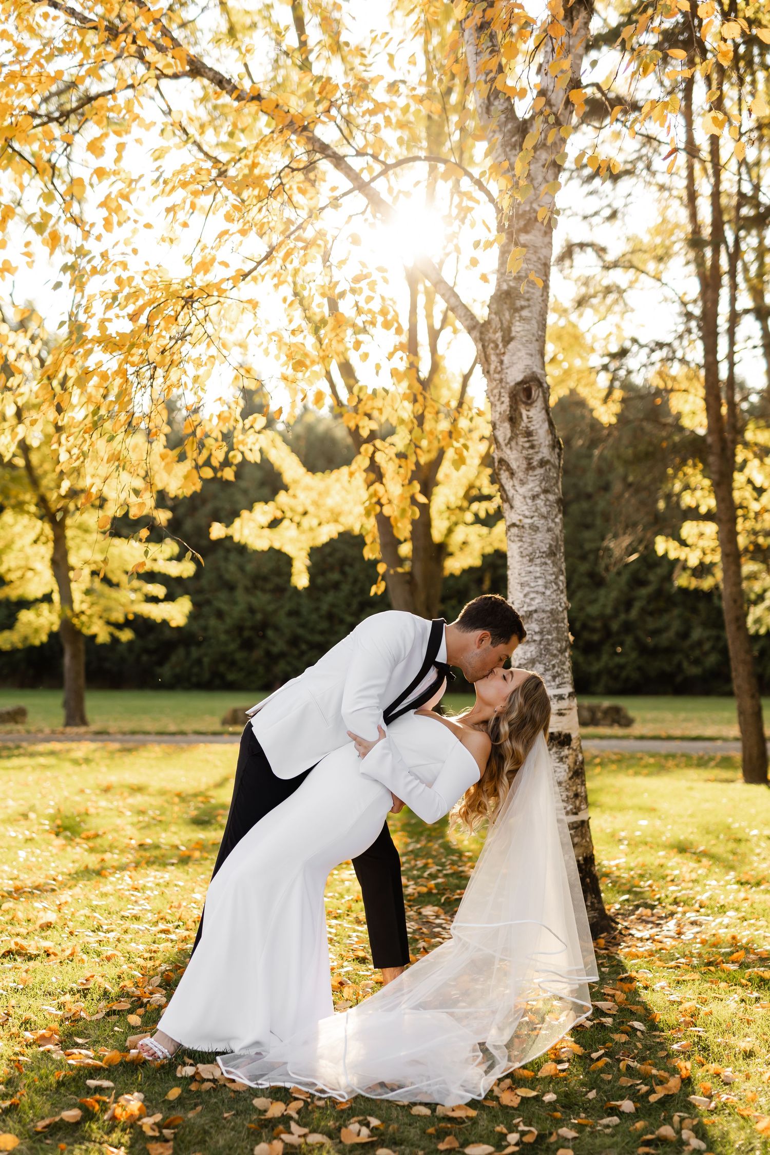 Couple shares romantic dip pose during sunset wedding photoshoot among autumn trees.