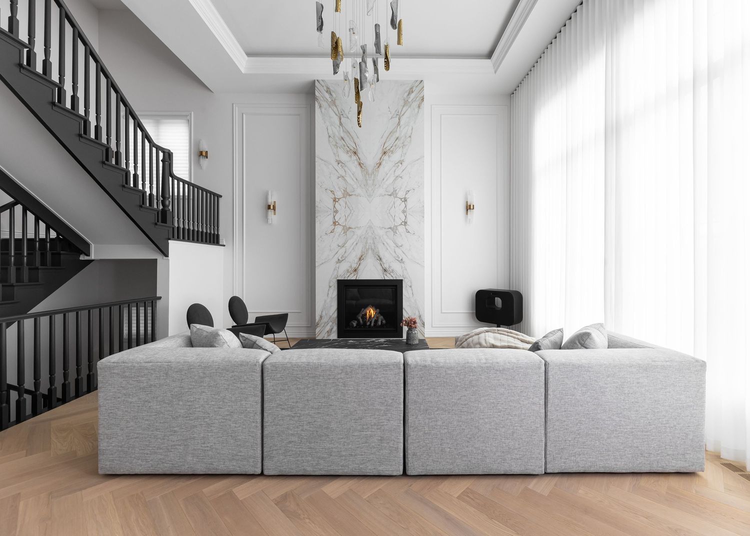 Contemporary living room with black staircase, white walls, and grey modular seating.