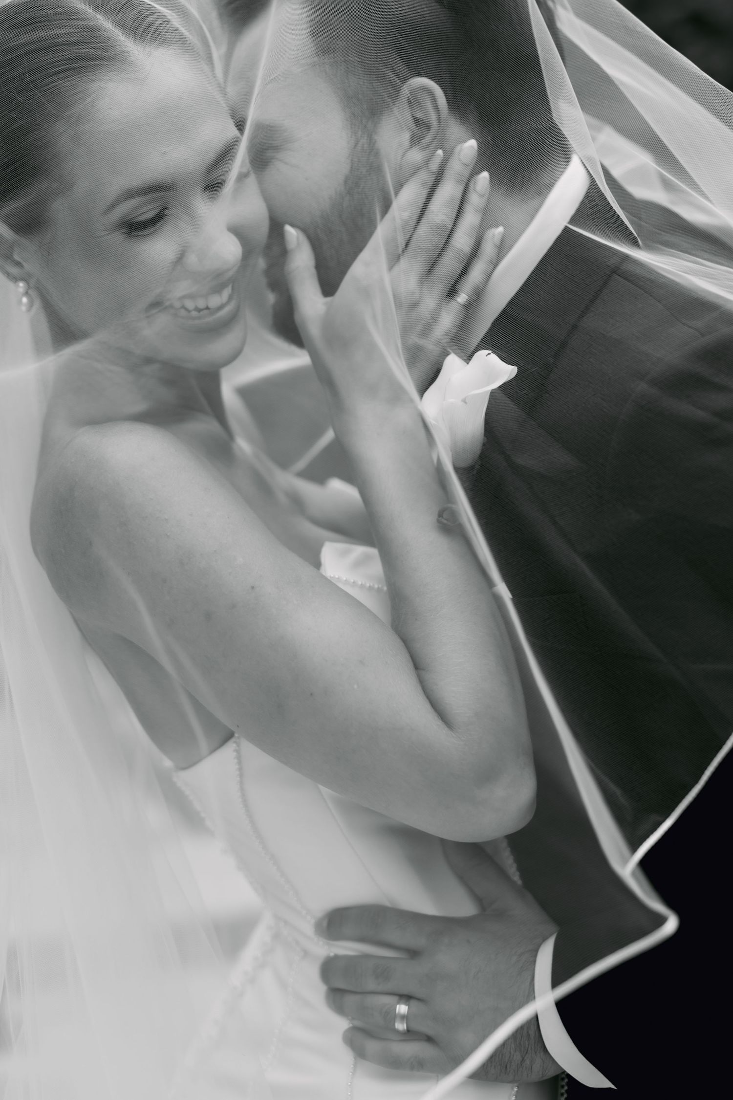 Black and white romantic wedding photo of bride and groom embracing under a veil.
