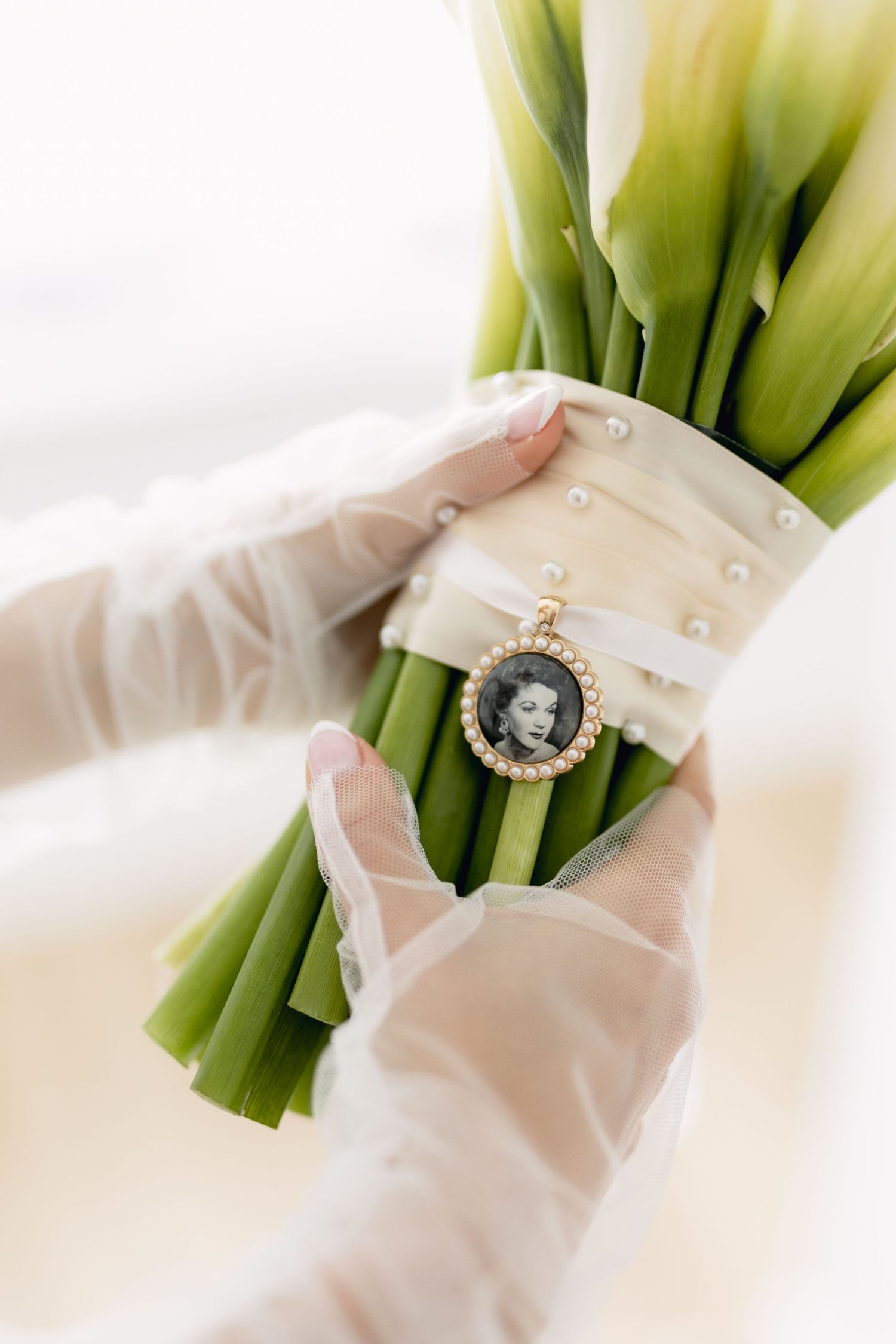 Bride holds tulip bouquet wrapped in pearl ribbon with vintage gold locket photo charm.