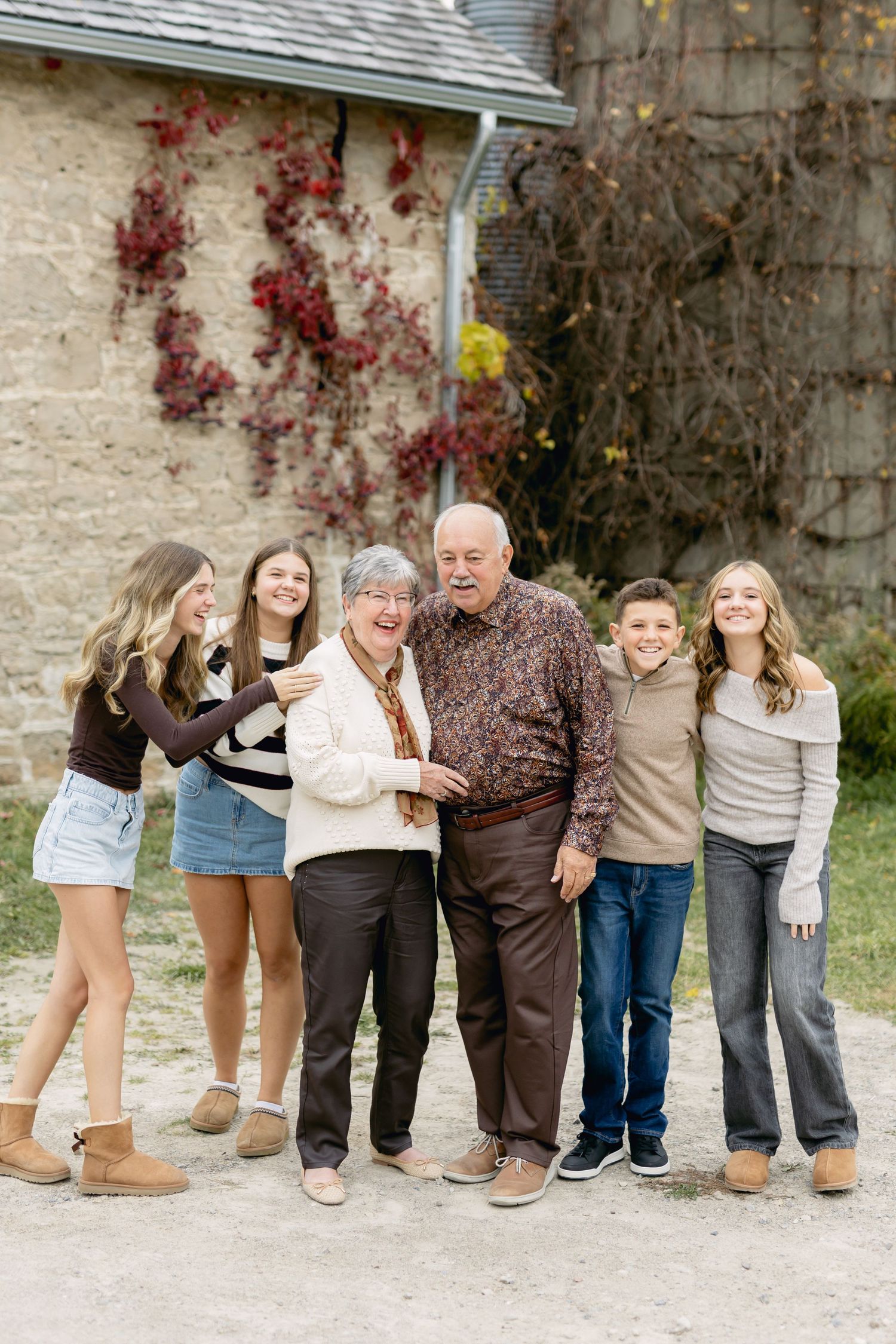 A multi-generational group poses casually against a stone wall with climbing vines.