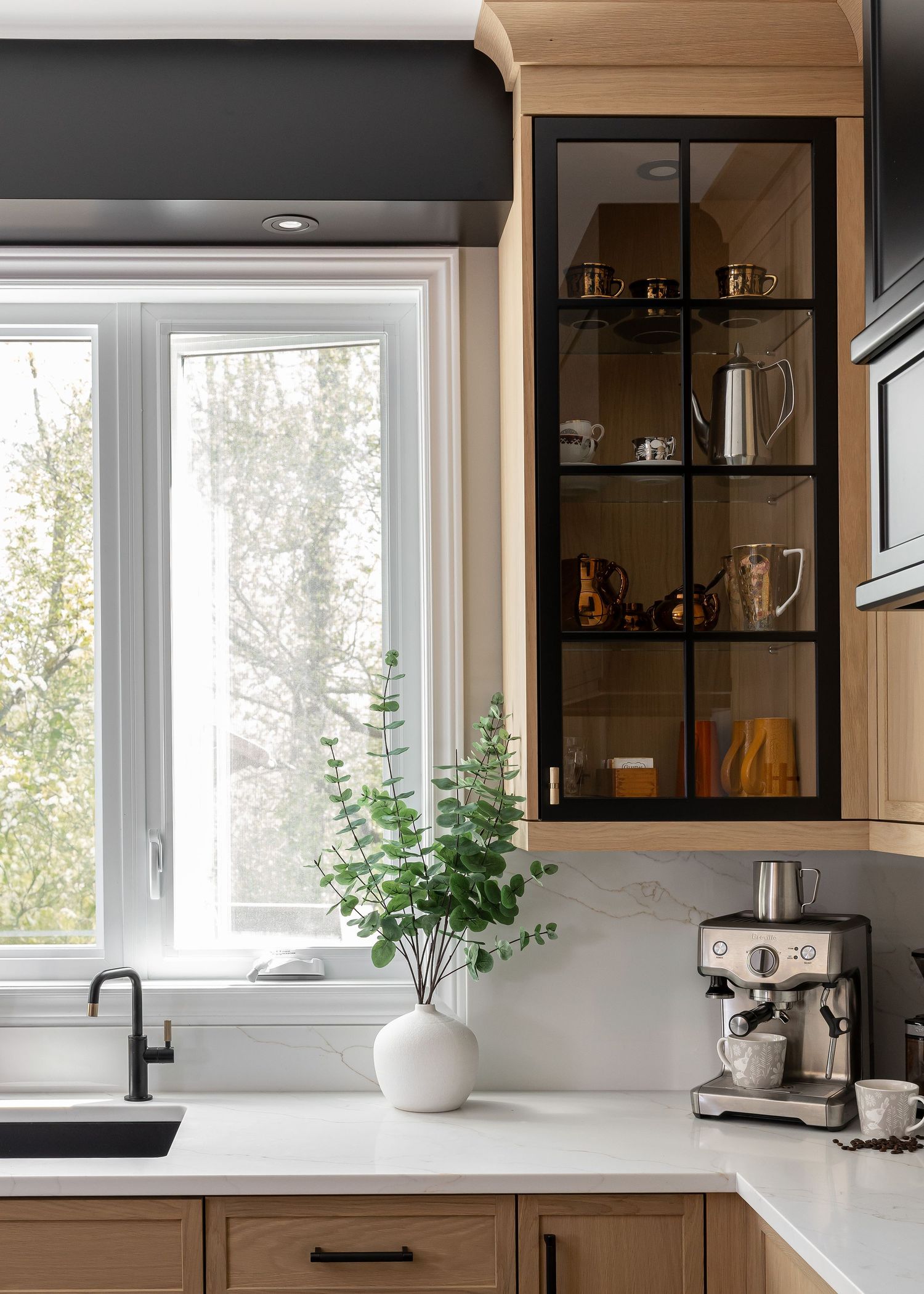 Modern kitchen with light wood cabinets, black accents, and white countertops featuring a window with natural lighting.