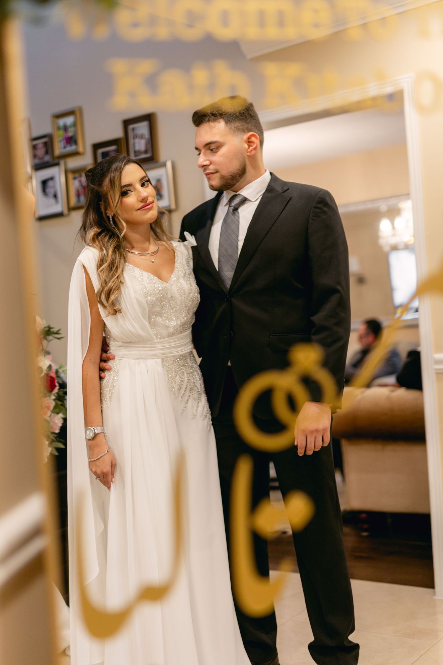 Wedding couple posing in front of decorative gold lettering and white drapes.