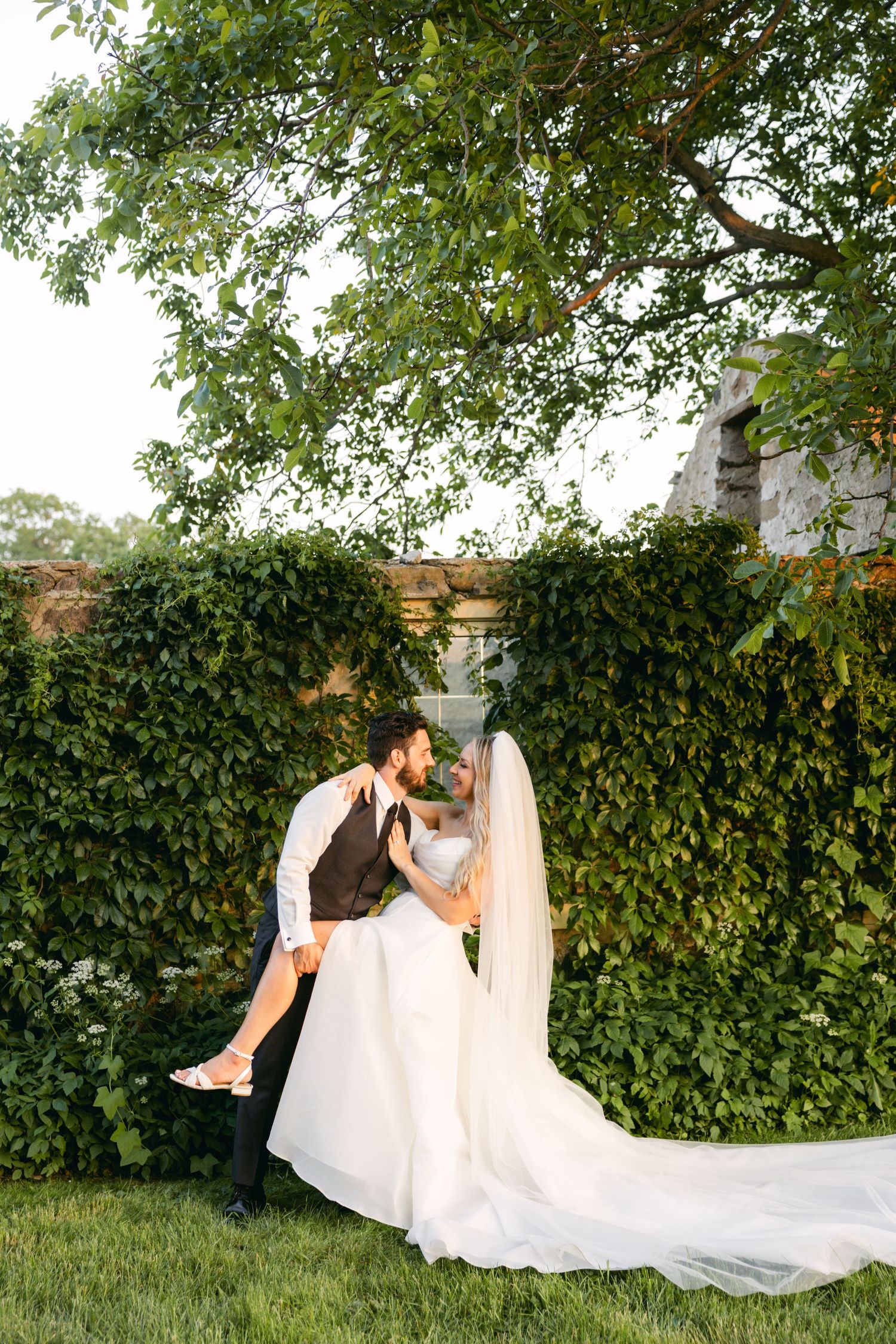 Wedding portraits against ivy-covered wall with flowing white dress train.