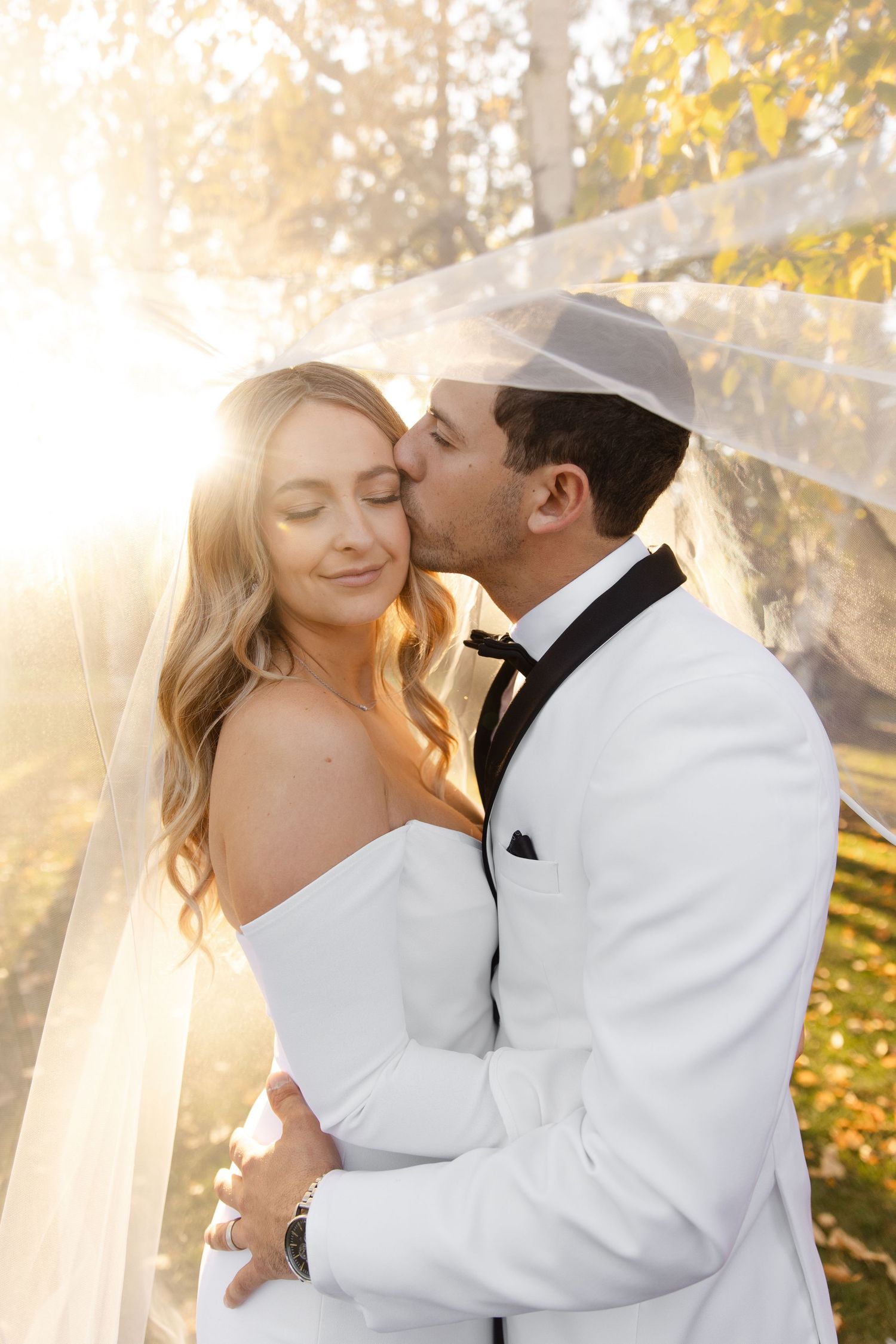 Romantic wedding portraits in golden sunlight with flowing white veil and formal attire.